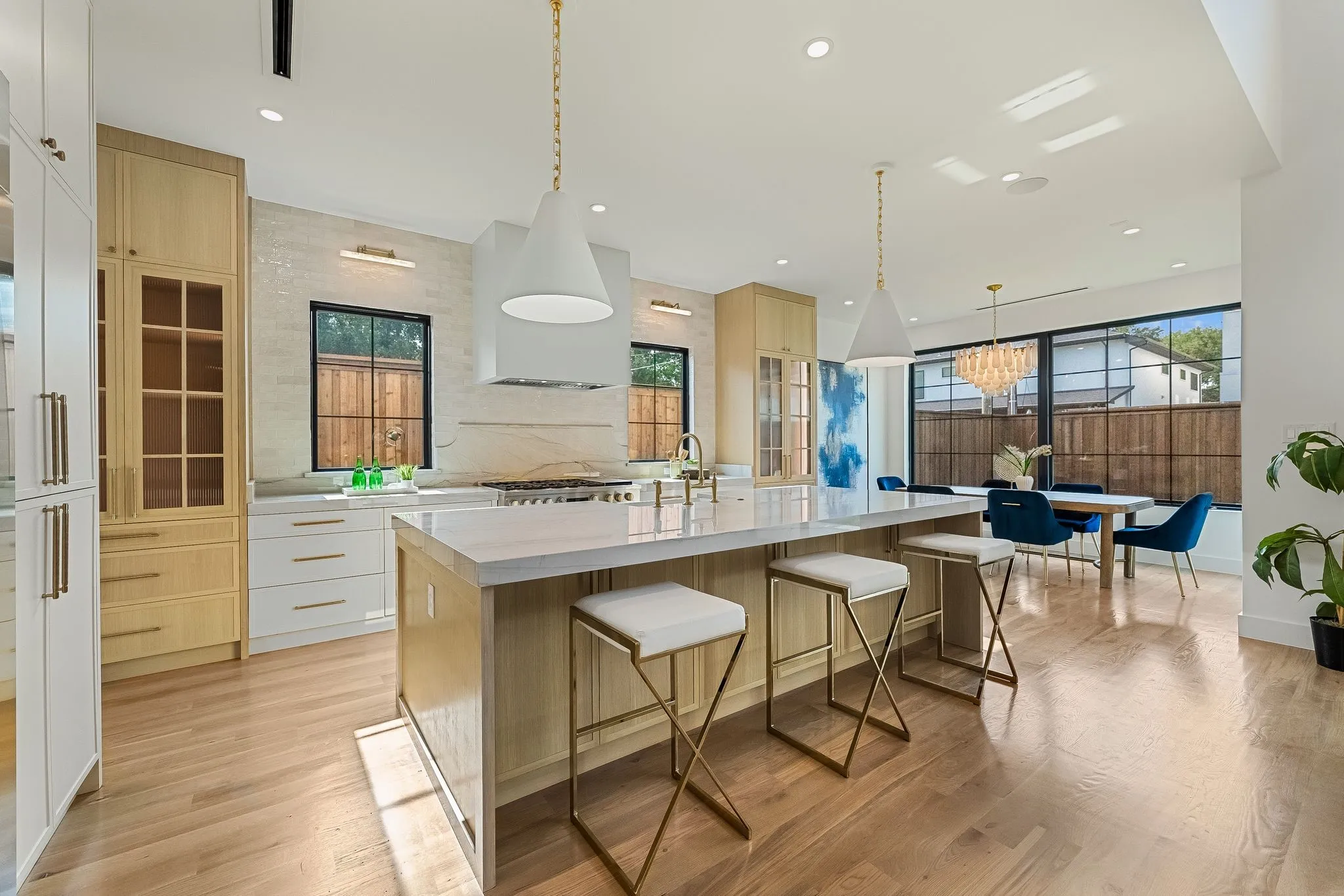Spacious open-concept kitchen featuring light wood-finish flooring, a large central island with seating, pendant lighting, built-in cabinetry with glass-front accents, and a dining area with a chandelier