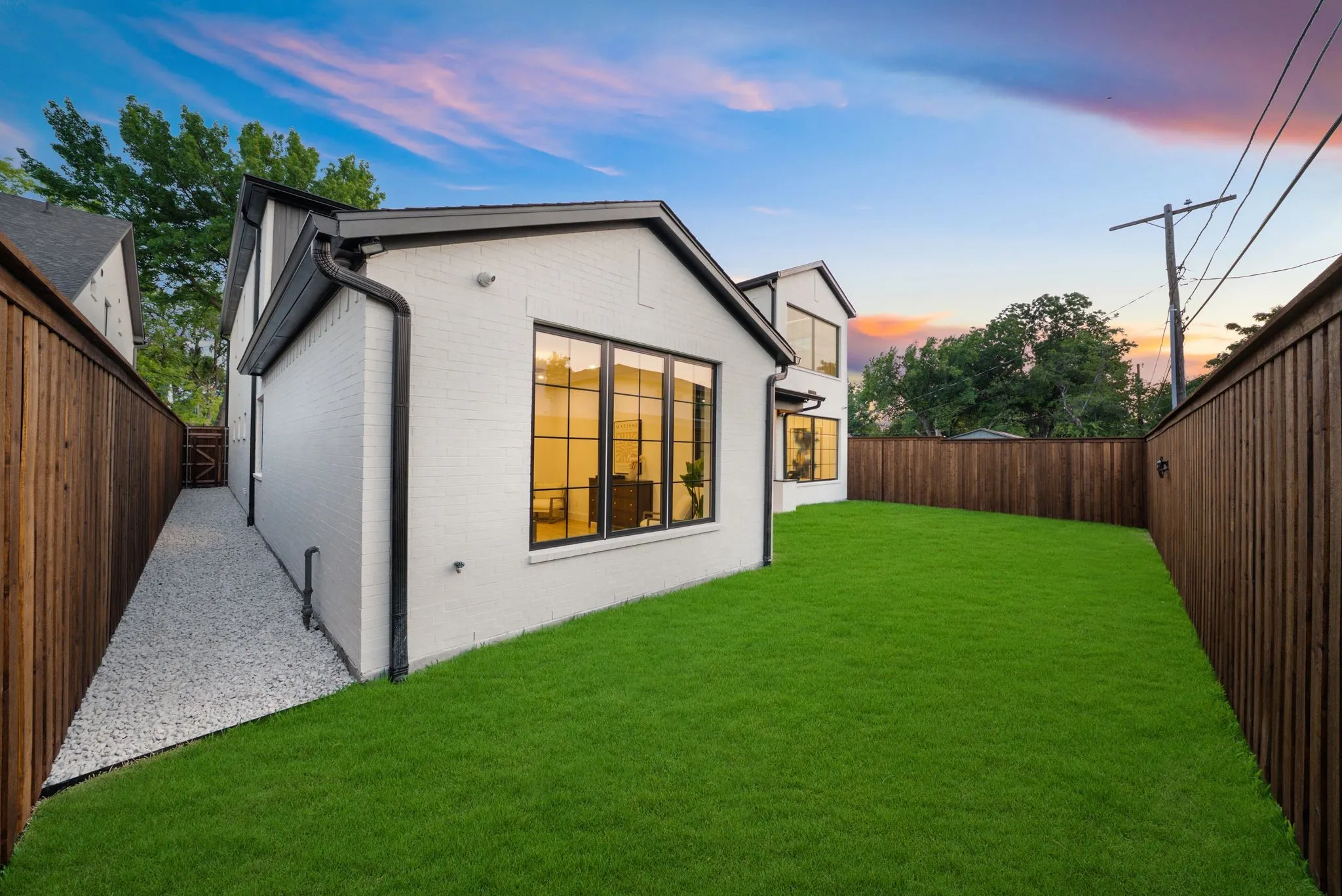 Modern residence featuring a spacious backyard with lush manicured lawn, mature landscaping, and wood-finish privacy fencing