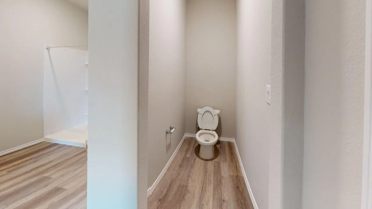 Bathroom space featuring wood-finish flooring, a white toilet, and a white shower stall with built-in shelving