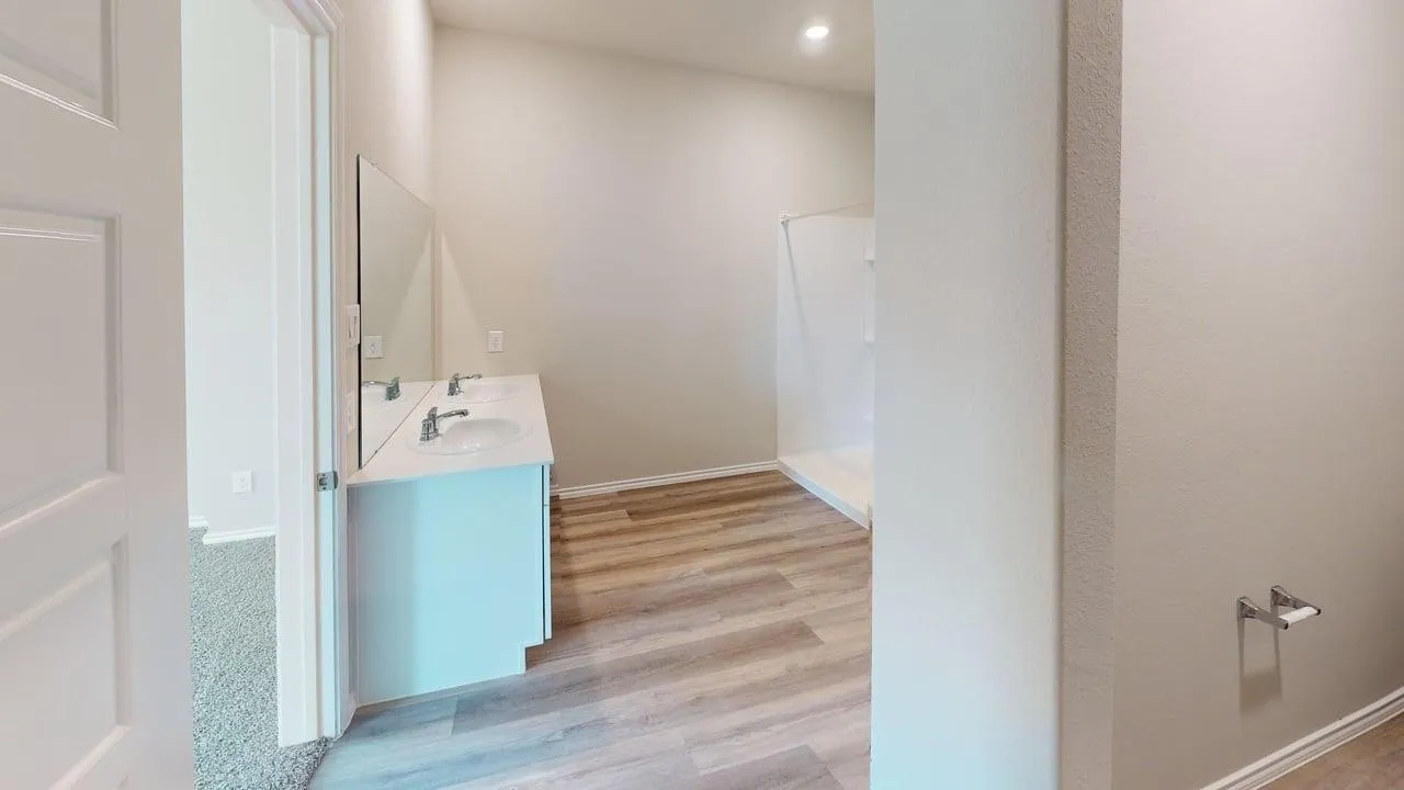 Modern bathroom featuring a light blue vanity with integrated sink and faucet, wood-finish flooring throughout, recessed ceiling lighting, and a spacious layout with glass shower enclosure