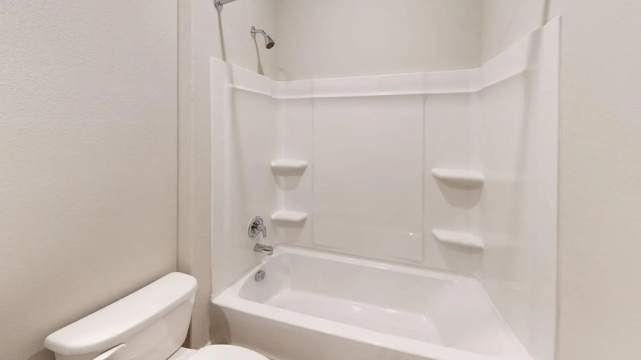 White bathtub and shower combination with chrome fixtures and integrated shelving