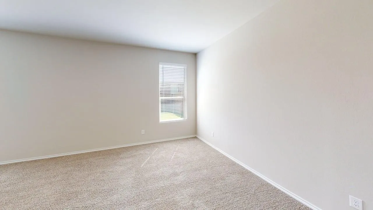 Spacious room featuring neutral carpeting, light-toned walls, and a single window with horizontal blinds