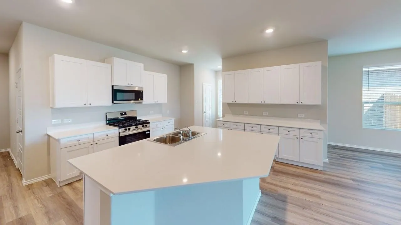 Bright kitchen featuring white shaker-style cabinetry, a central island with an undermount double basin stainless steel sink, stainless steel gas range with overhead microwave, and wood-finish flooring