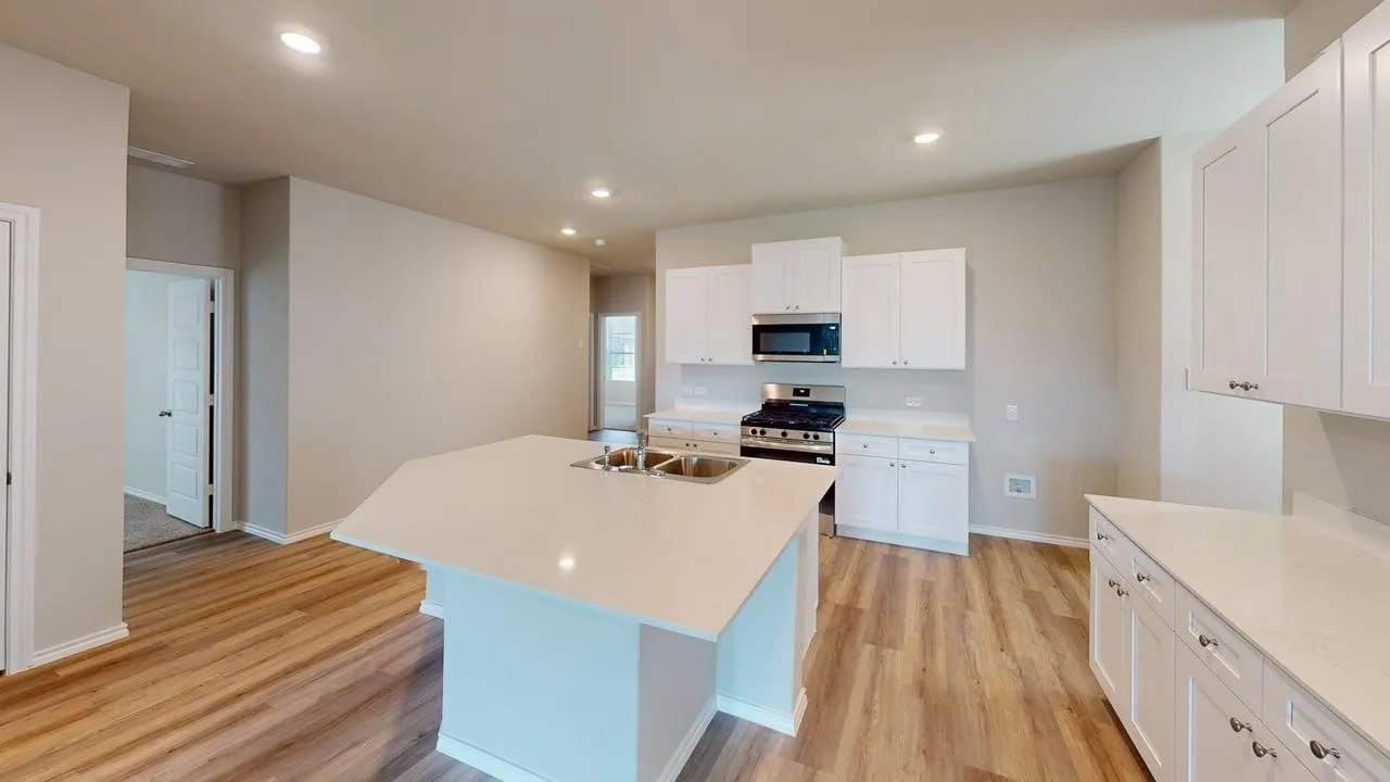 Modern kitchen featuring an angled island with an undermount sink, white shaker-style cabinetry, stainless steel appliances, and light wood-finish flooring