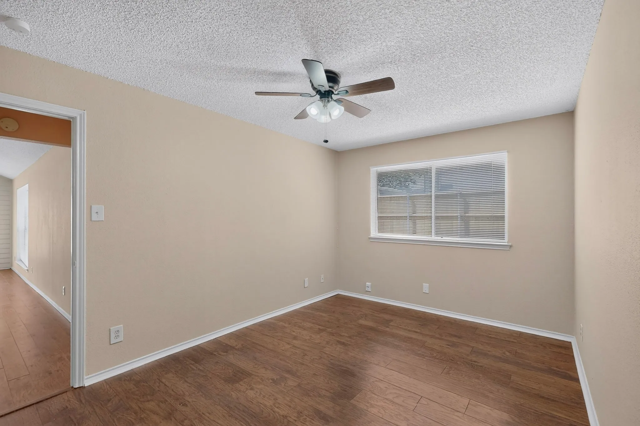 Wood-finish flooring, neutral wall color, ceiling fan with integrated lighting, and a double-hung window
