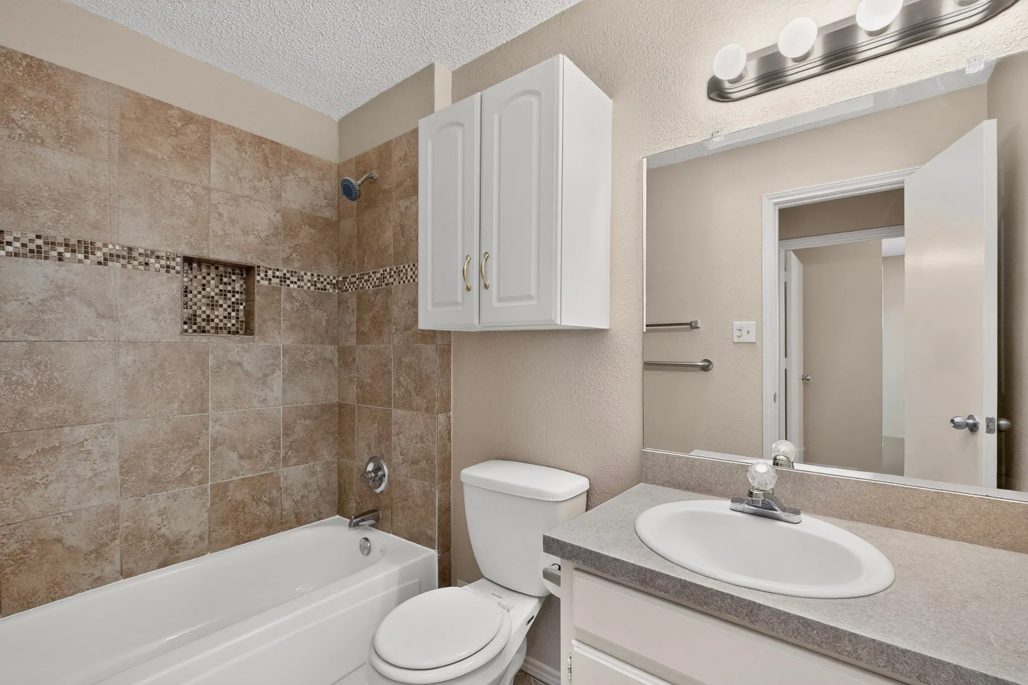 Bathroom featuring a tiled shower surround with a decorative mosaic accent and recessed niche, white bathtub, built-in vanity with an integrated sink, and wall-mounted mirror