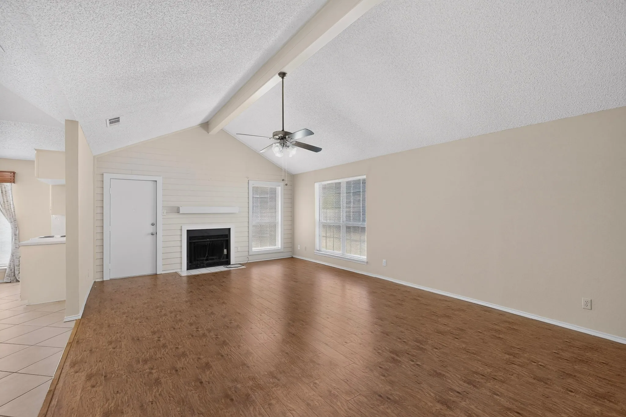 Vaulted ceiling with exposed beam, wood-finish flooring, fireplace with mantel, ceiling fan, and multiple windows