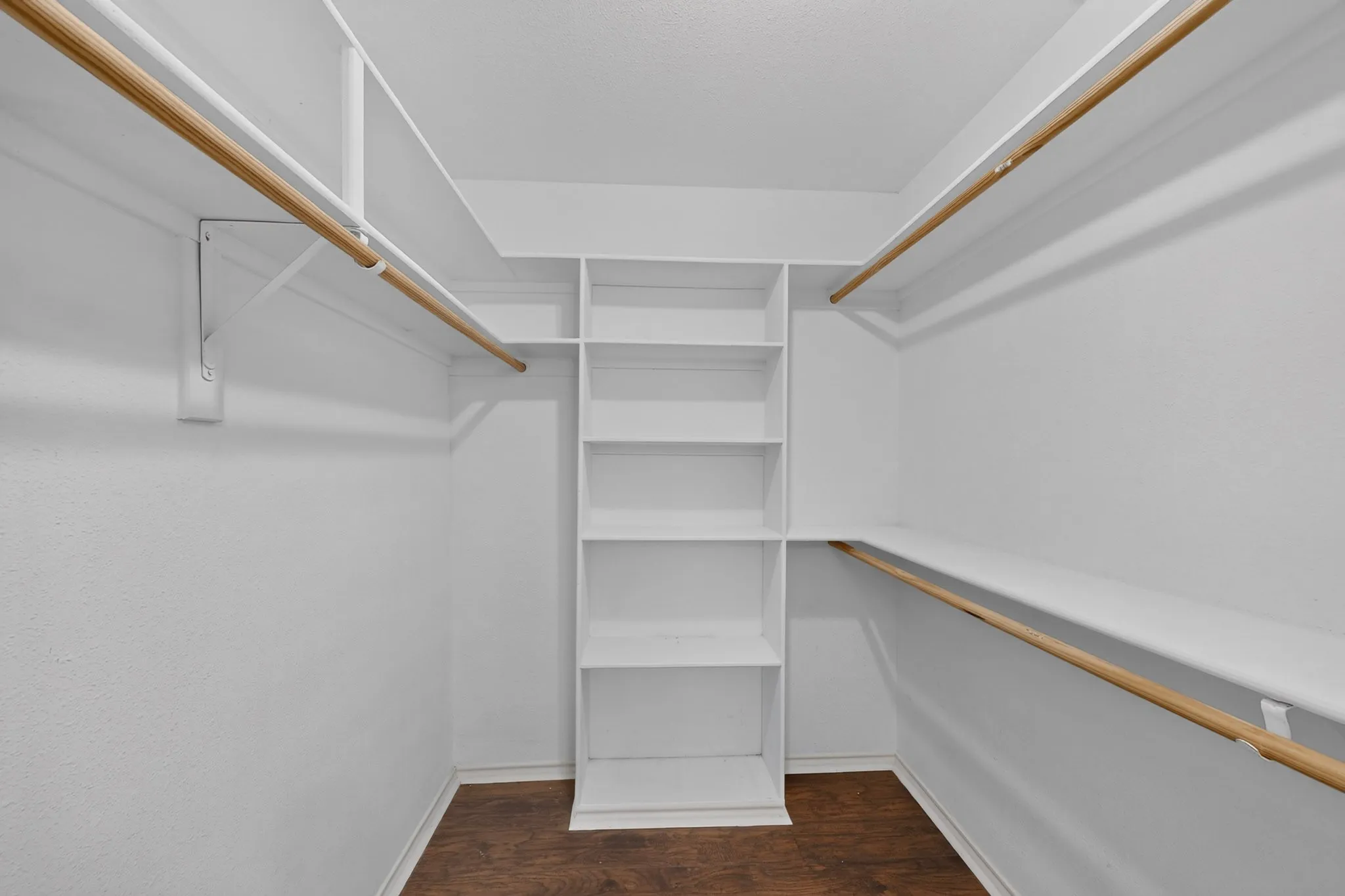 Built-in shelving and hanging rods for organized storage within this closet space, featuring wood-finish flooring