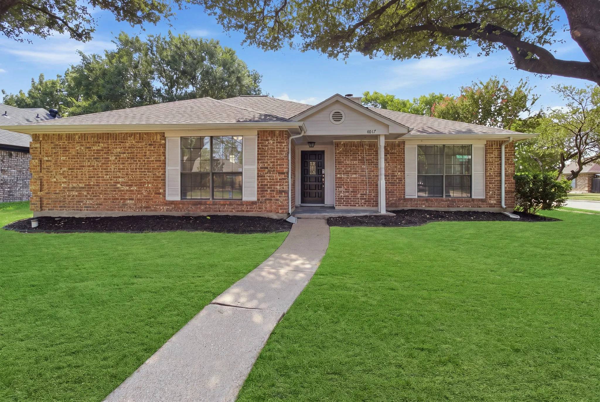 Brick facade home with a gabled entry, featuring a shingled roof, white window shutters, and a front walkway