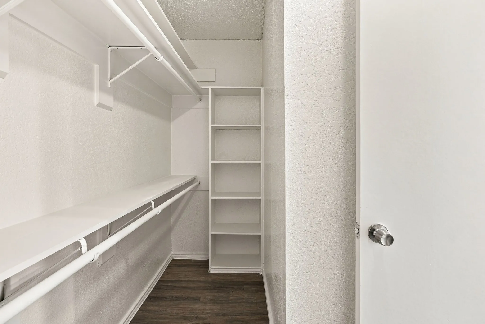Walk-in closet featuring white wire shelving, hanging rods, and dark wood-finish flooring