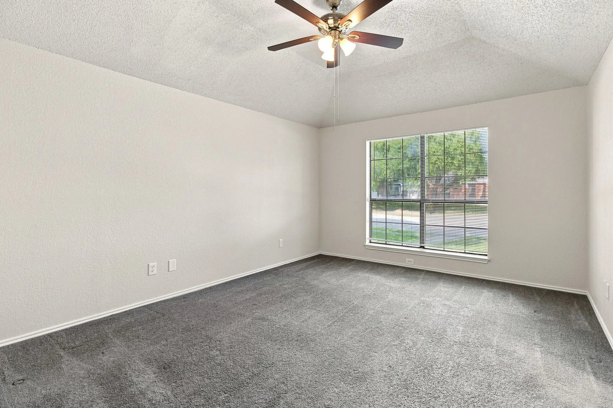 Spacious room featuring neutral-toned walls, gray textured carpeting, and a ceiling fan with integrated lighting