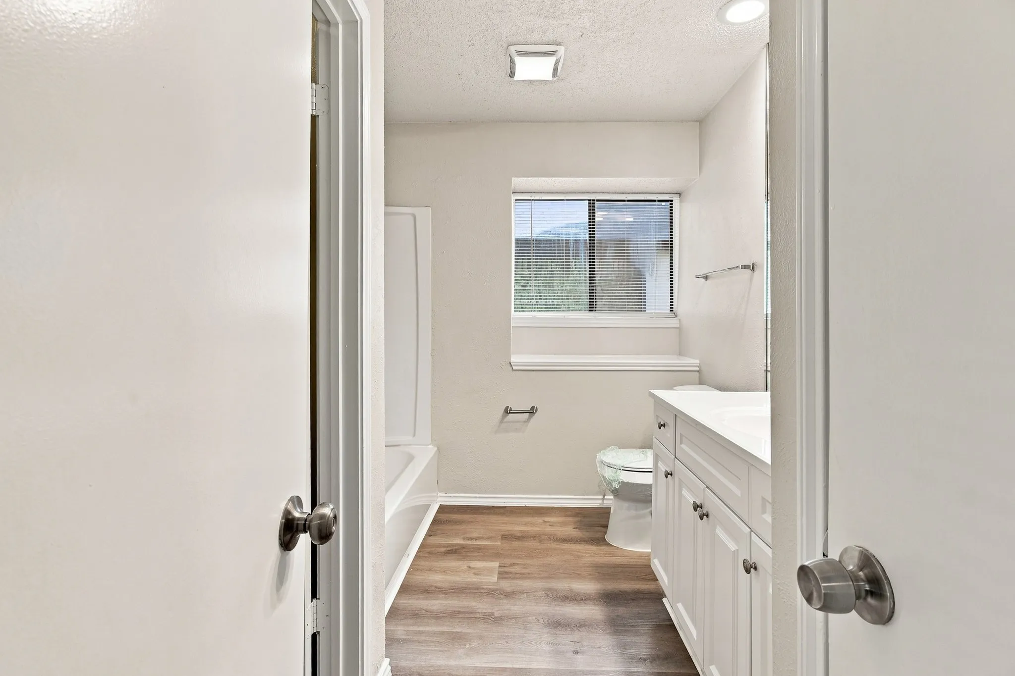 Elegant primary bathroom showcasing white cabinetry with brushed nickel hardware, a wood-finish vanity with dual sink configuration, and white subway tile surround