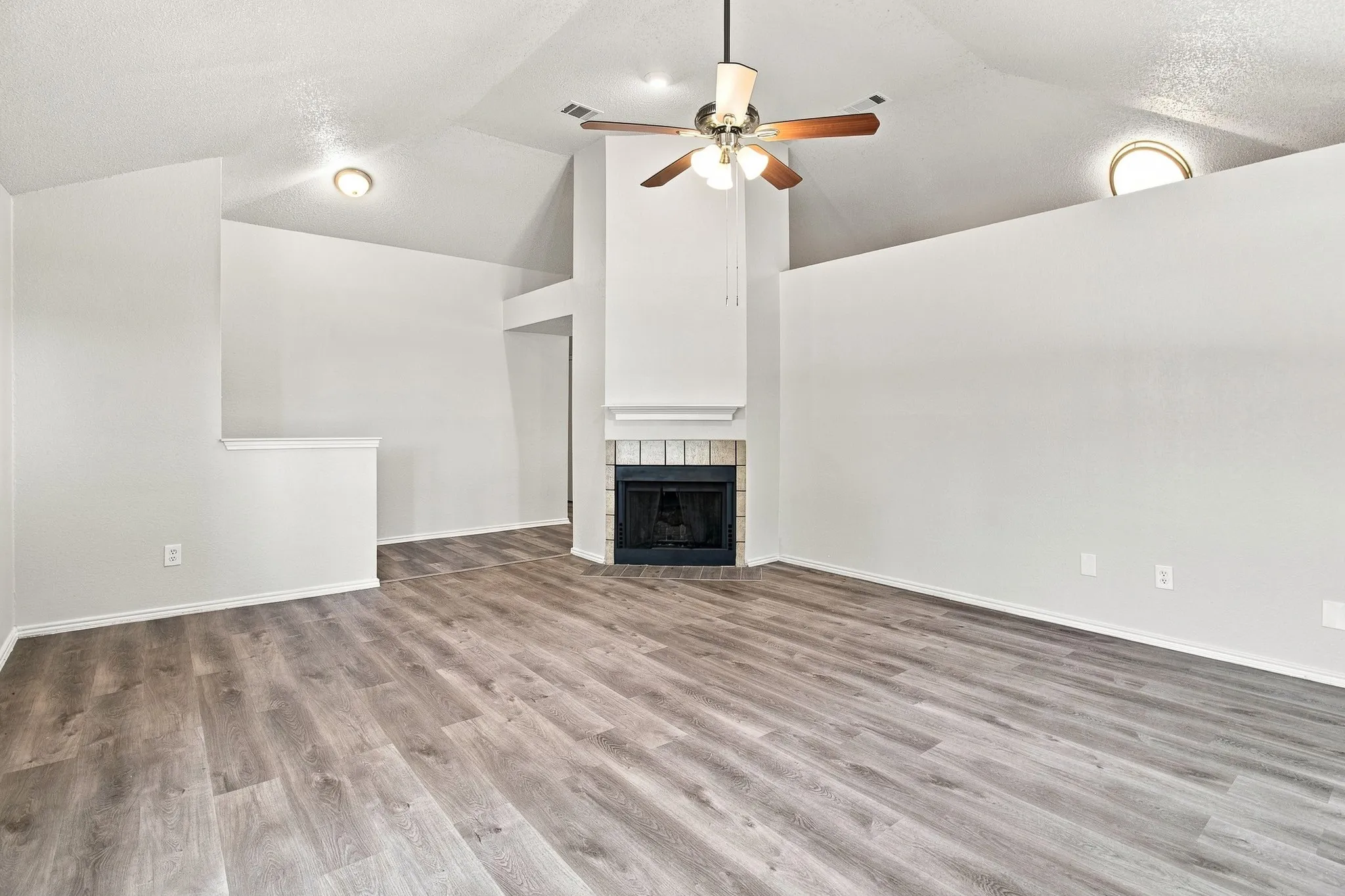 Spacious living area featuring wood-finish flooring, vaulted ceilings, a corner fireplace with tile surround, a ceiling fan, and recessed lighting