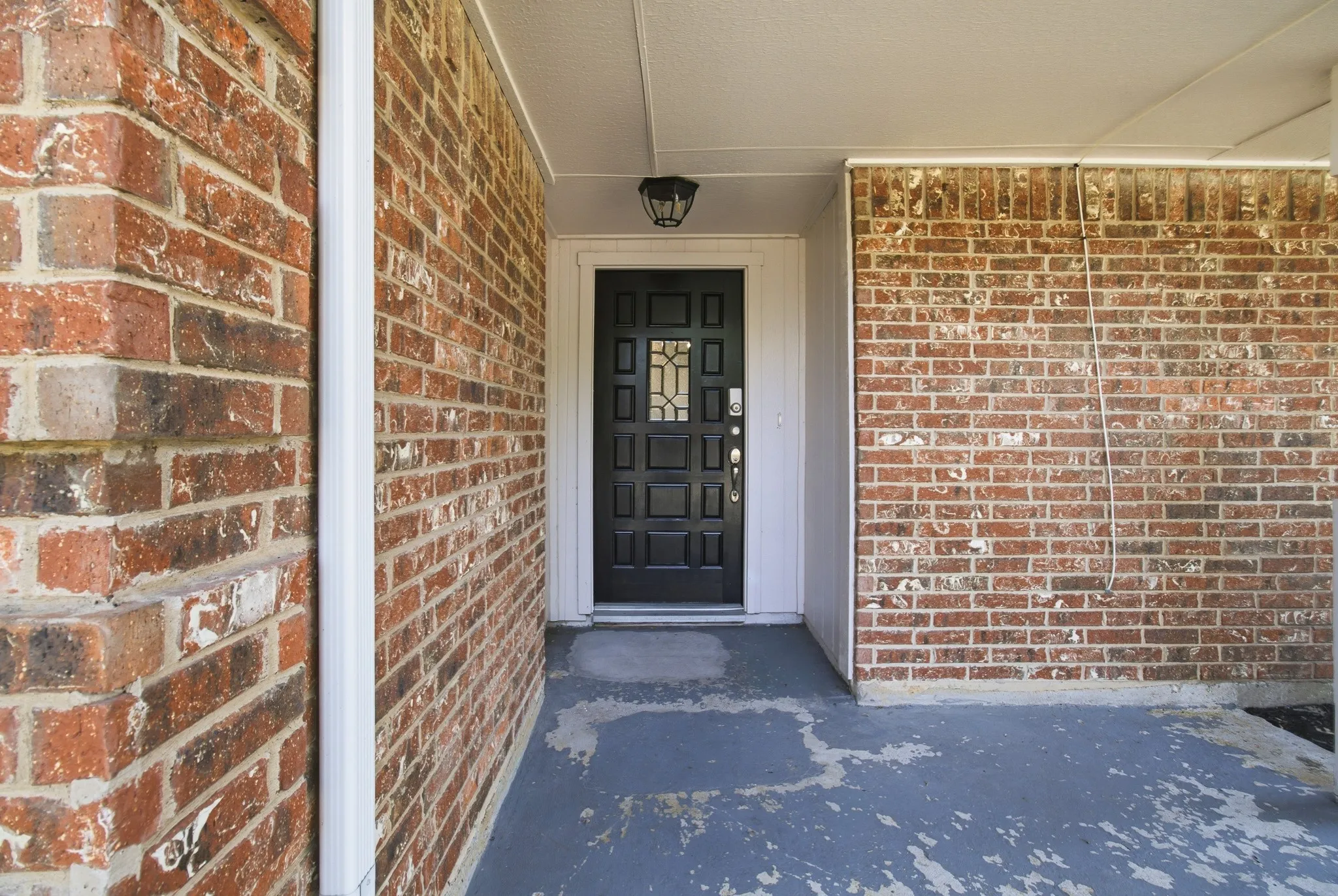 Brick facade entry featuring a dark paneled door with decorative glass inserts and overhead lighting