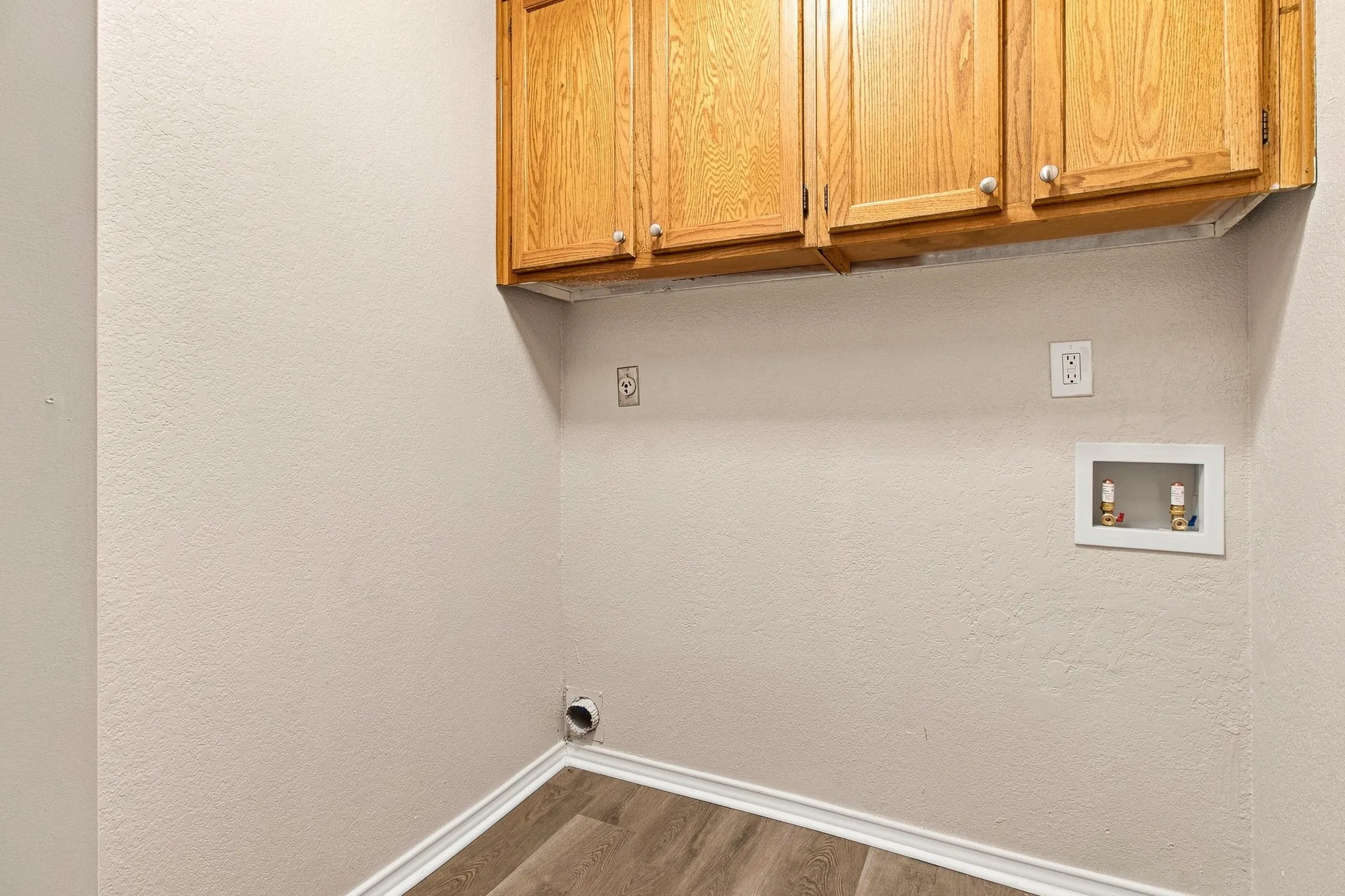 Utility area with wood-finish flooring, light-toned walls, overhead cabinetry, and laundry hookups