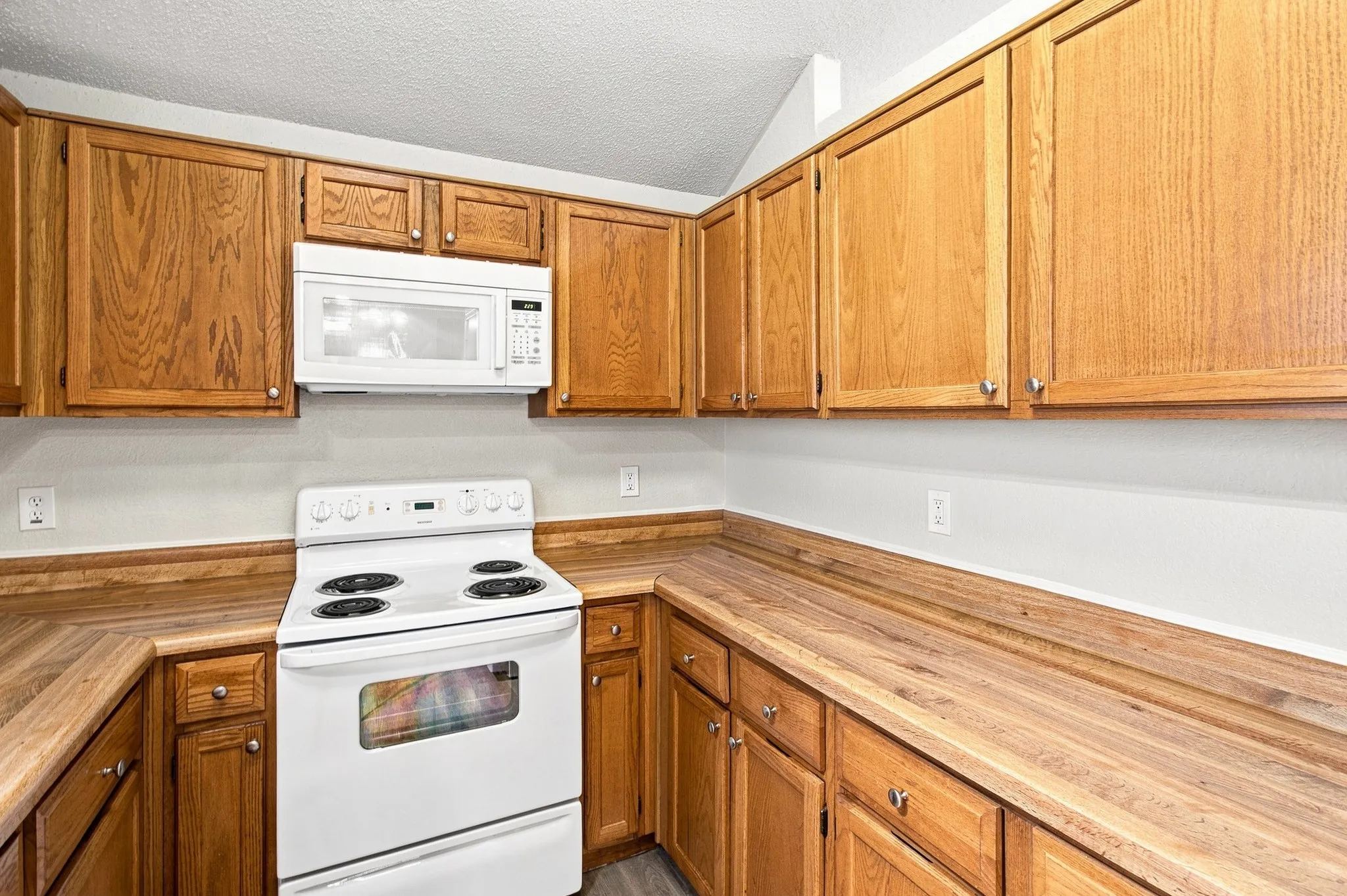 Kitchen featuring wood-finish cabinetry, wood-look countertops, and a white electric range with an overhead microwave