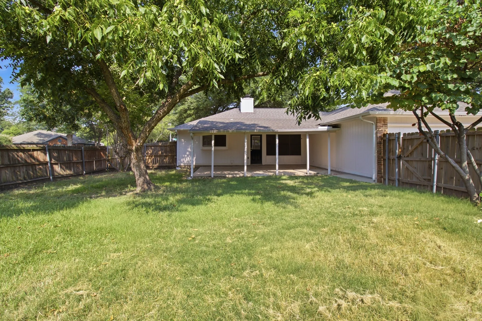Spacious backyard featuring a covered patio, mature shade trees, and a full privacy fence