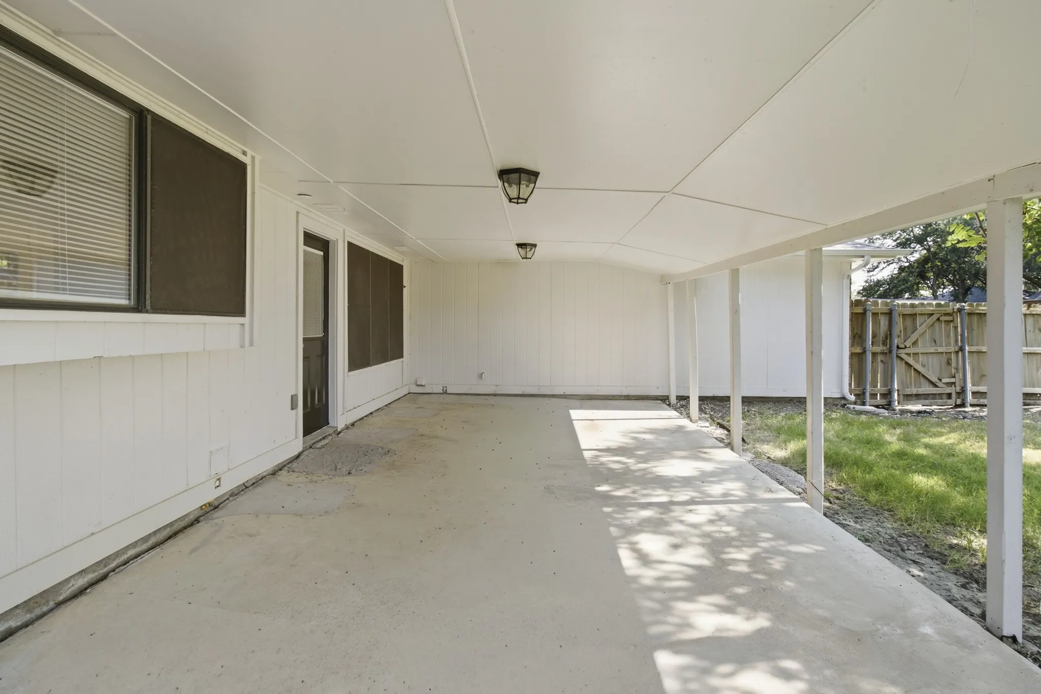 Expansive covered patio with concrete flooring, supported by multiple white pillars, featuring recessed lighting fixtures