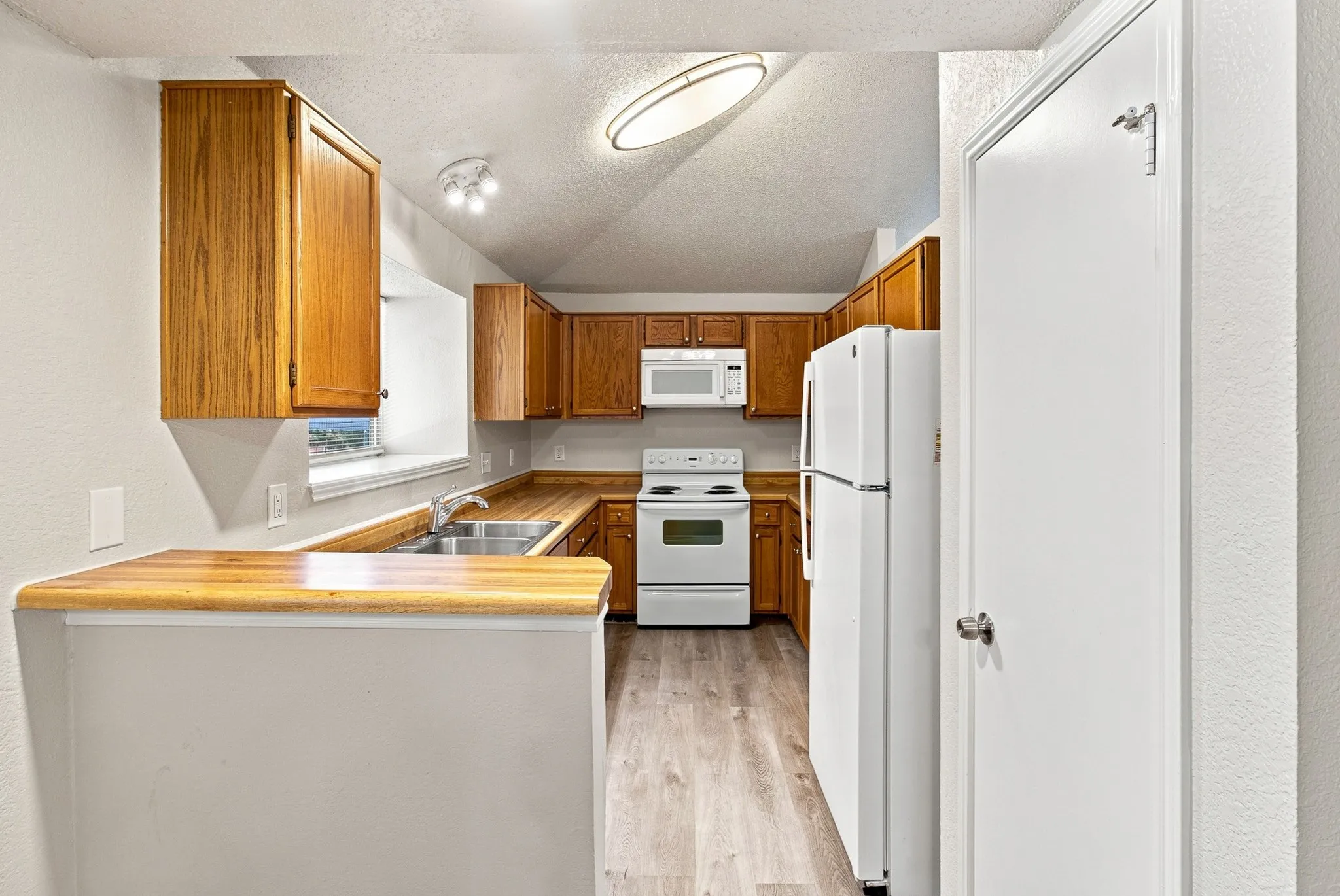 Kitchen featuring wood-finish cabinetry, wood-finish countertops, stainless steel double basin sink, and white appliances