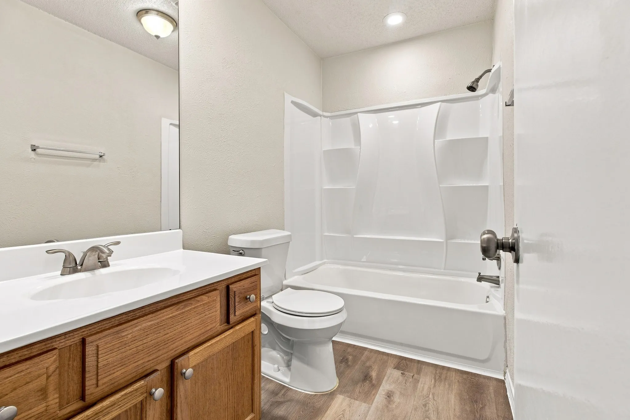 Bathroom featuring a wood-finish vanity with a white countertop, an integrated sink, a full-width mirror, and a white tub/shower combination with built-in shelving
