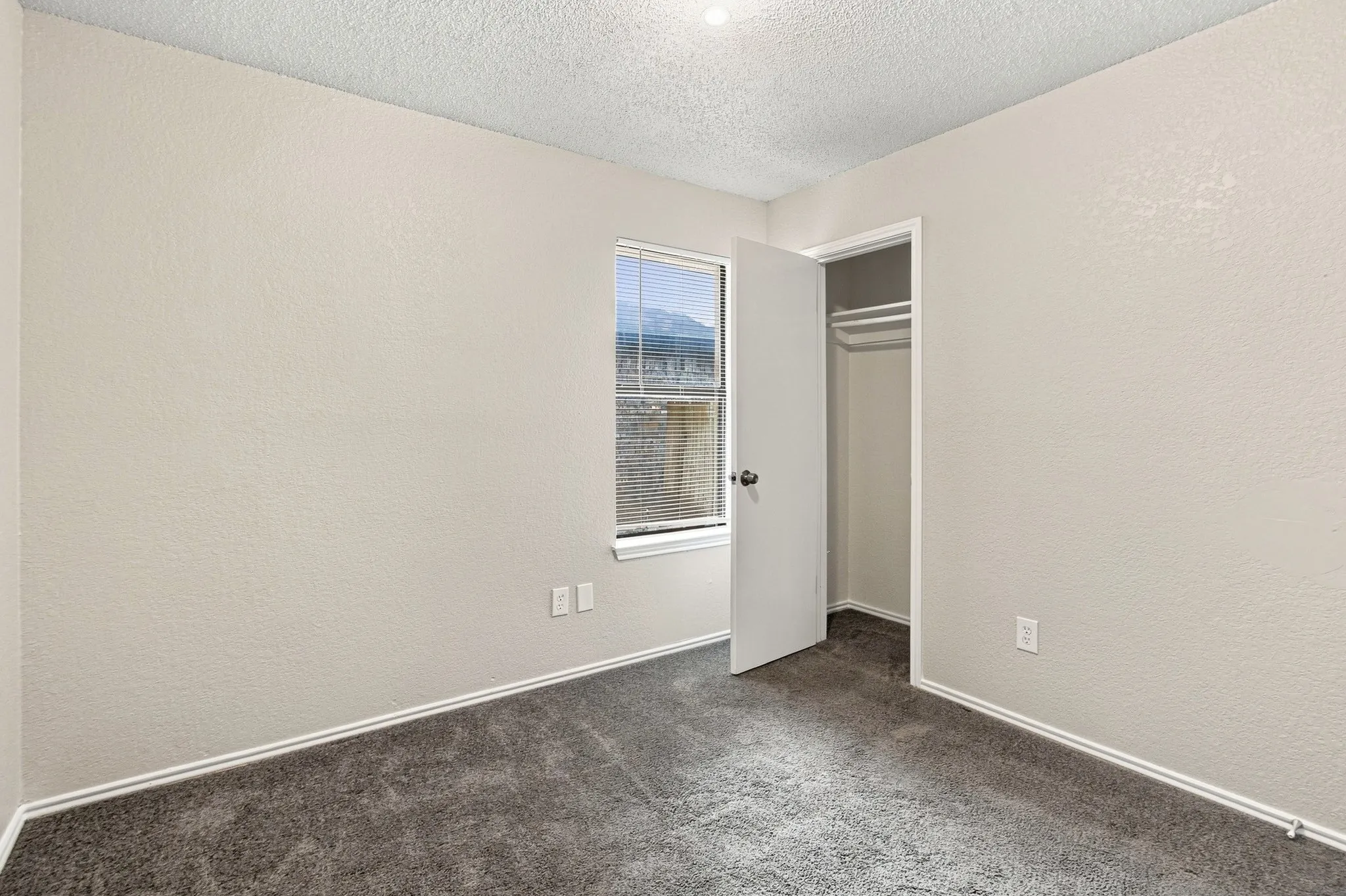 Bedroom featuring light gray wall paint, dark gray carpeting, a window with blinds, and a built-in closet with hanging rods