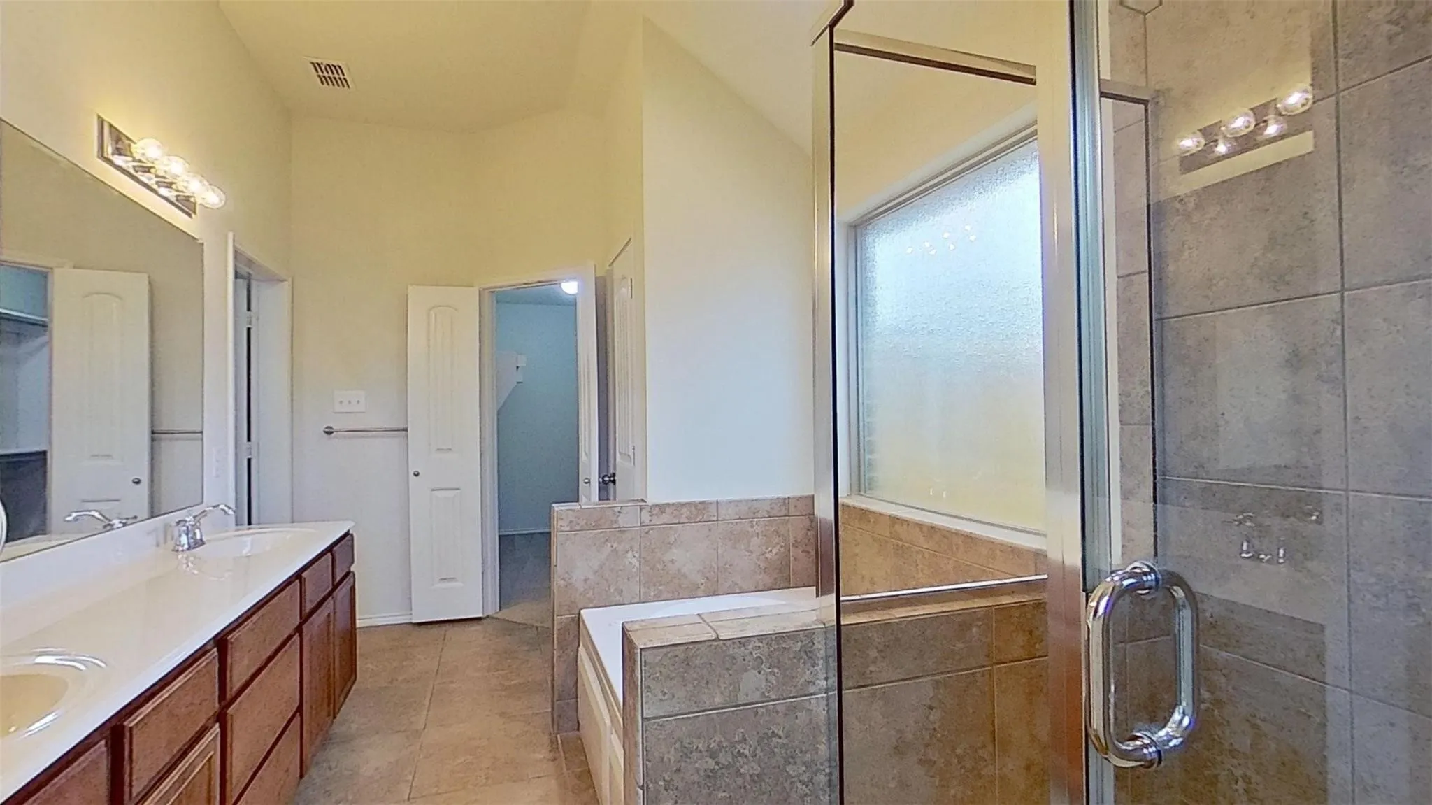 Bathroom featuring a dual vanity with wood cabinetry, a tiled soaking tub, and a separate glass-enclosed shower