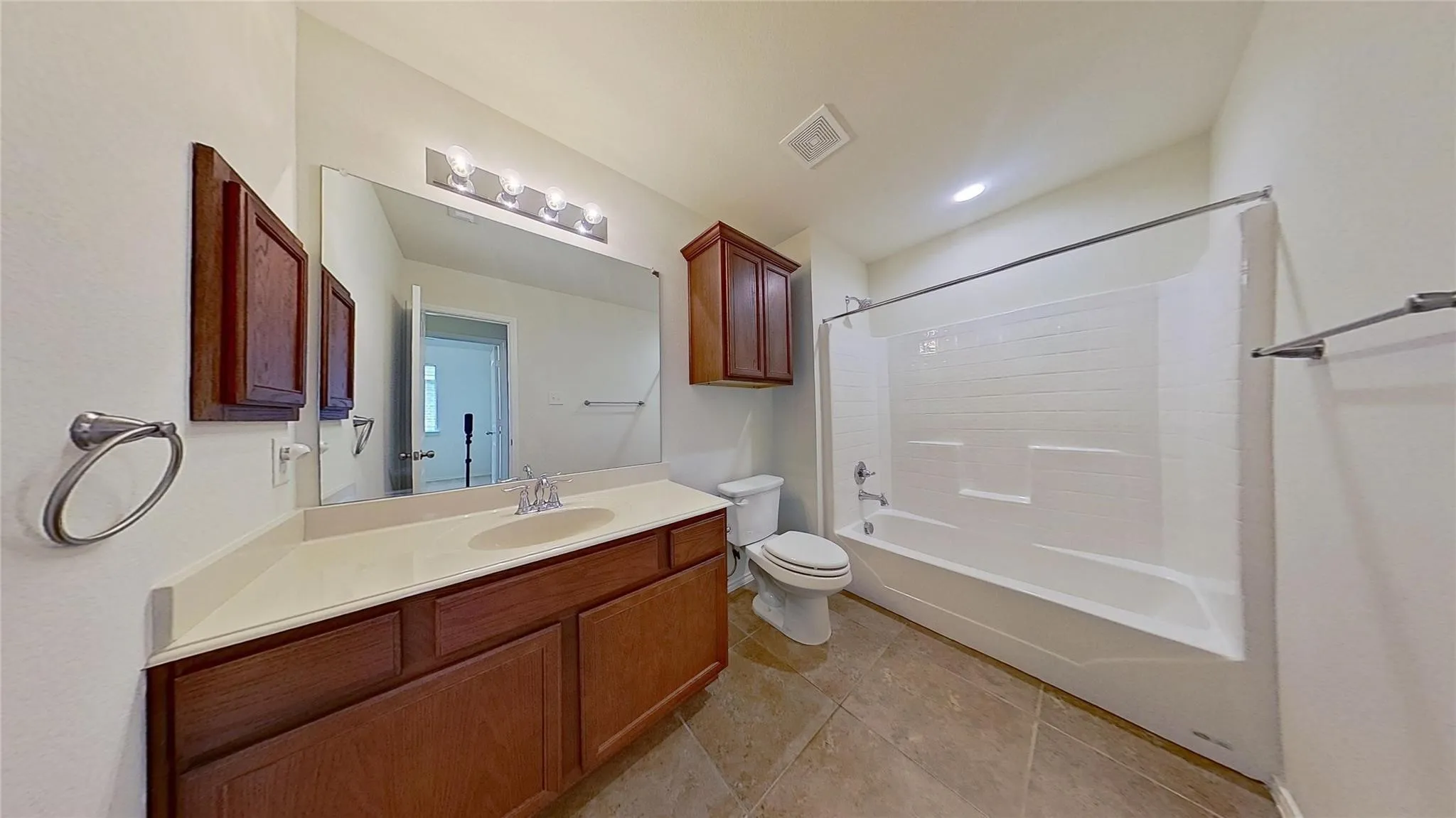 Bathroom featuring a spacious vanity with an integrated sink and light-toned countertop, extensive wall-mounted mirror, and a full-size bathtub with a shower