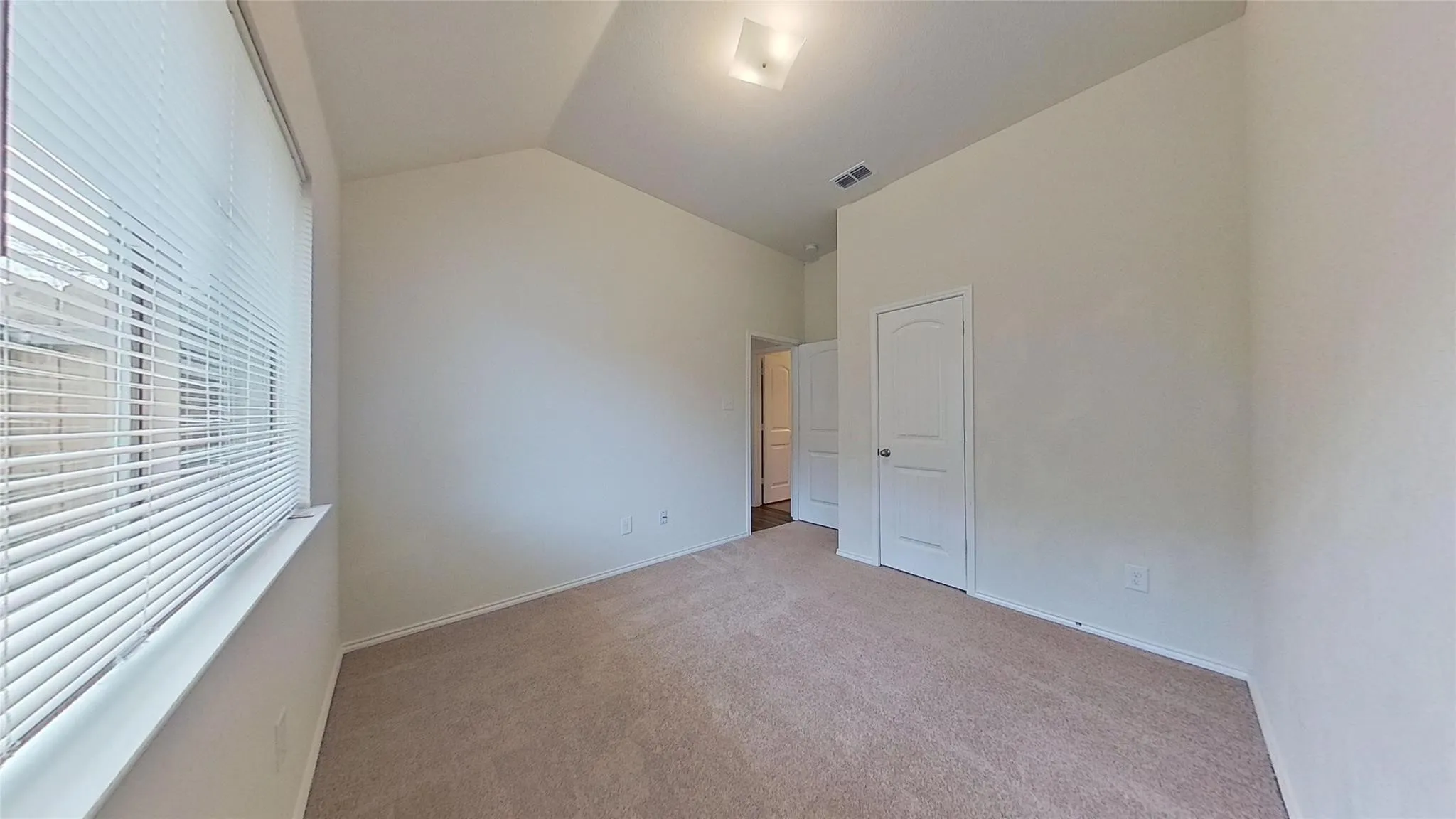 Spacious interior room featuring vaulted ceilings, neutral-toned carpet flooring, and a window with horizontal blinds