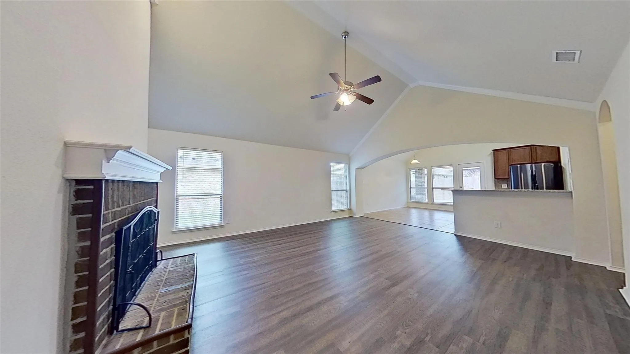 Spacious living area featuring high vaulted ceilings, wood-finish flooring, and a brick fireplace