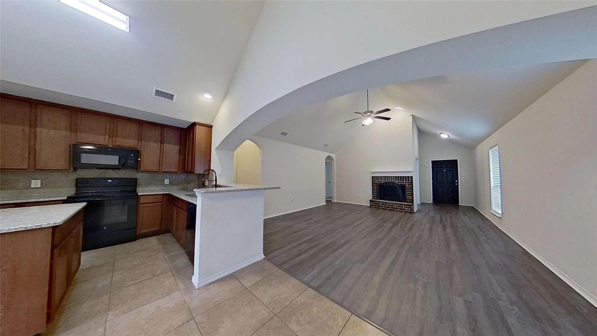 Open-concept living space with vaulted ceilings, a brick fireplace, and wood-finish flooring