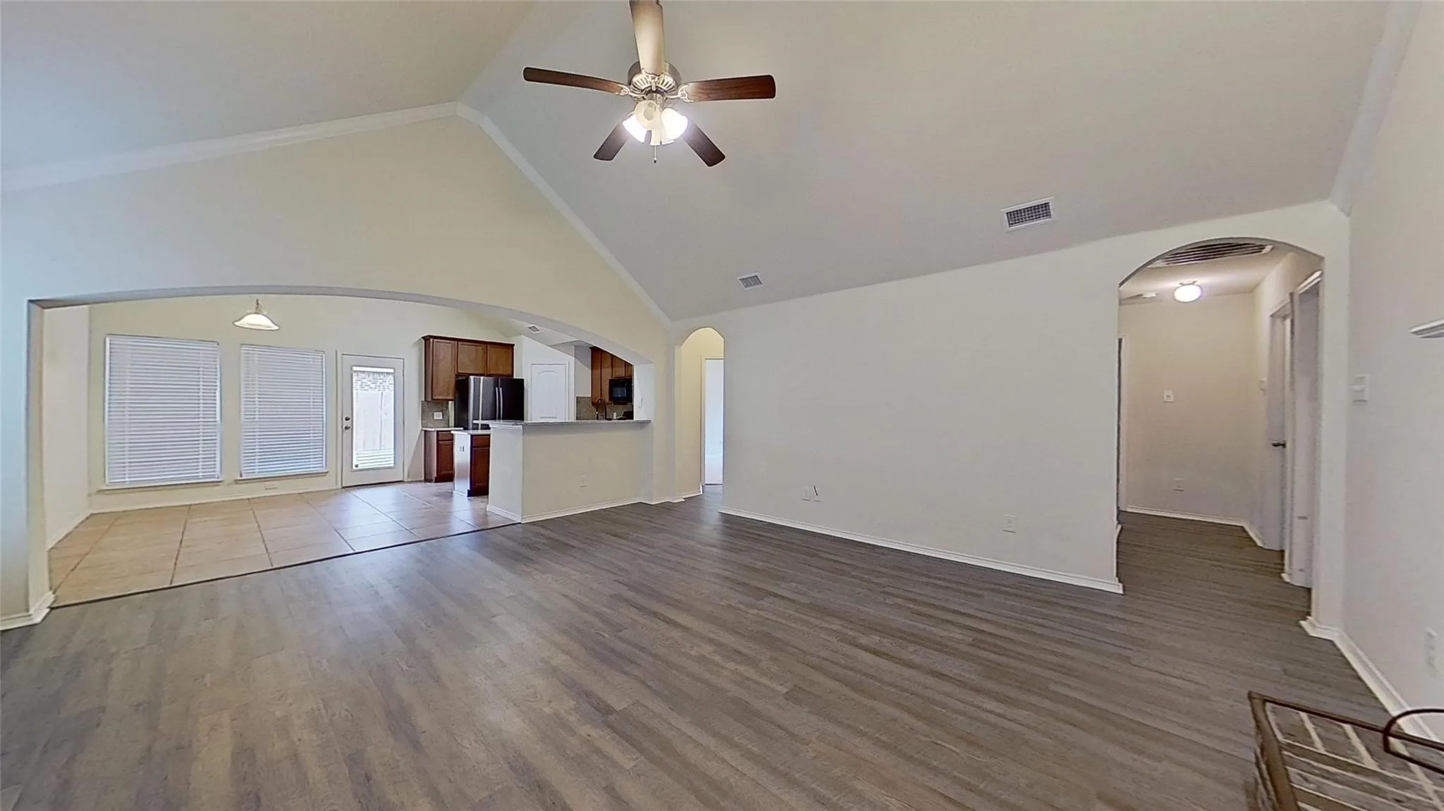 Vaulted ceiling living area featuring wood-finish flooring, a ceiling fan, and an arched entryway