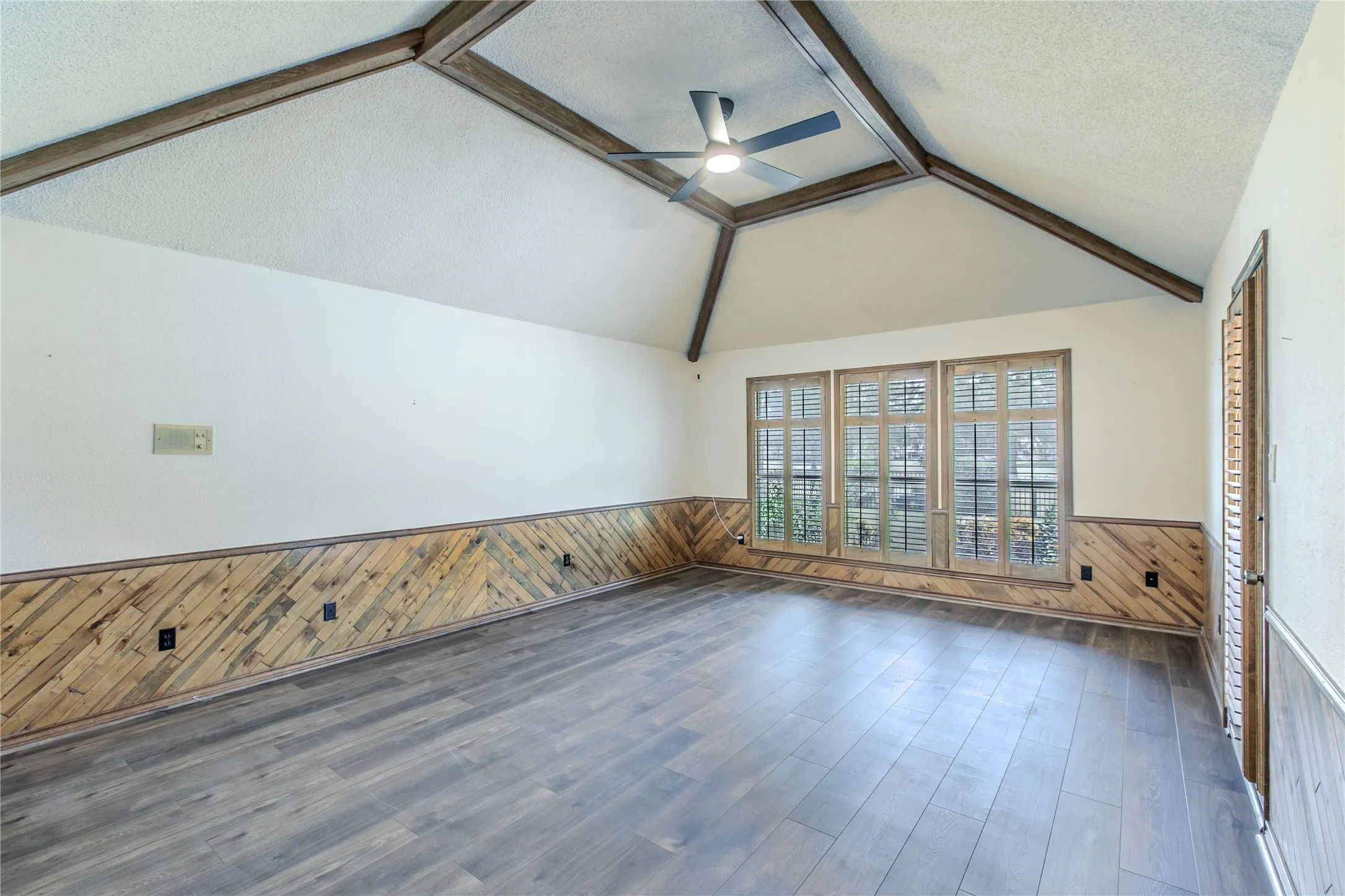 Spacious room featuring vaulted ceilings with exposed wood beams, a modern ceiling fan, wood-finish flooring, and wood paneling
