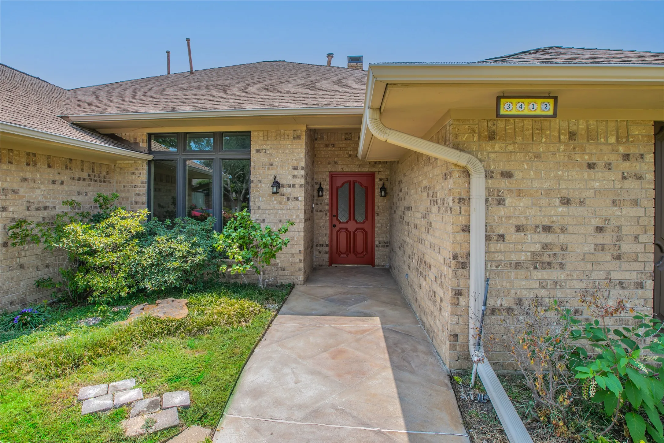 Brick exterior featuring a red entry door with glass inserts, transom window, and a concrete pathway