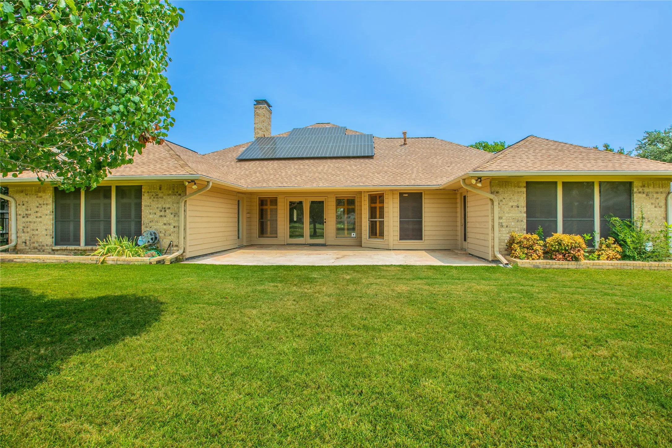 Expansive rear facade featuring a large patio, multiple window openings with screens, and a brick chimney