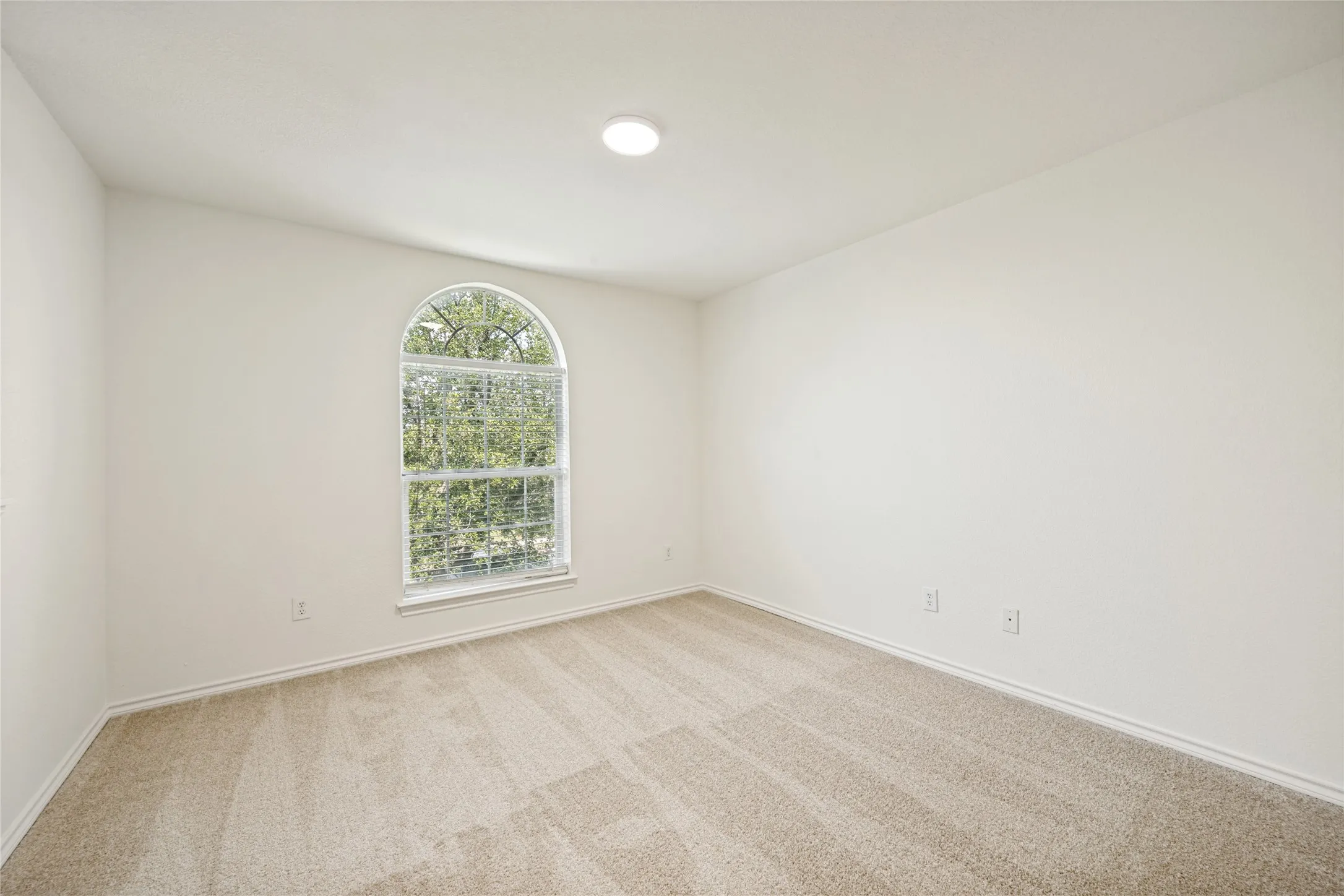 Bright interior space featuring a prominent arched window, neutral wall paint, recessed lighting, and carpet flooring