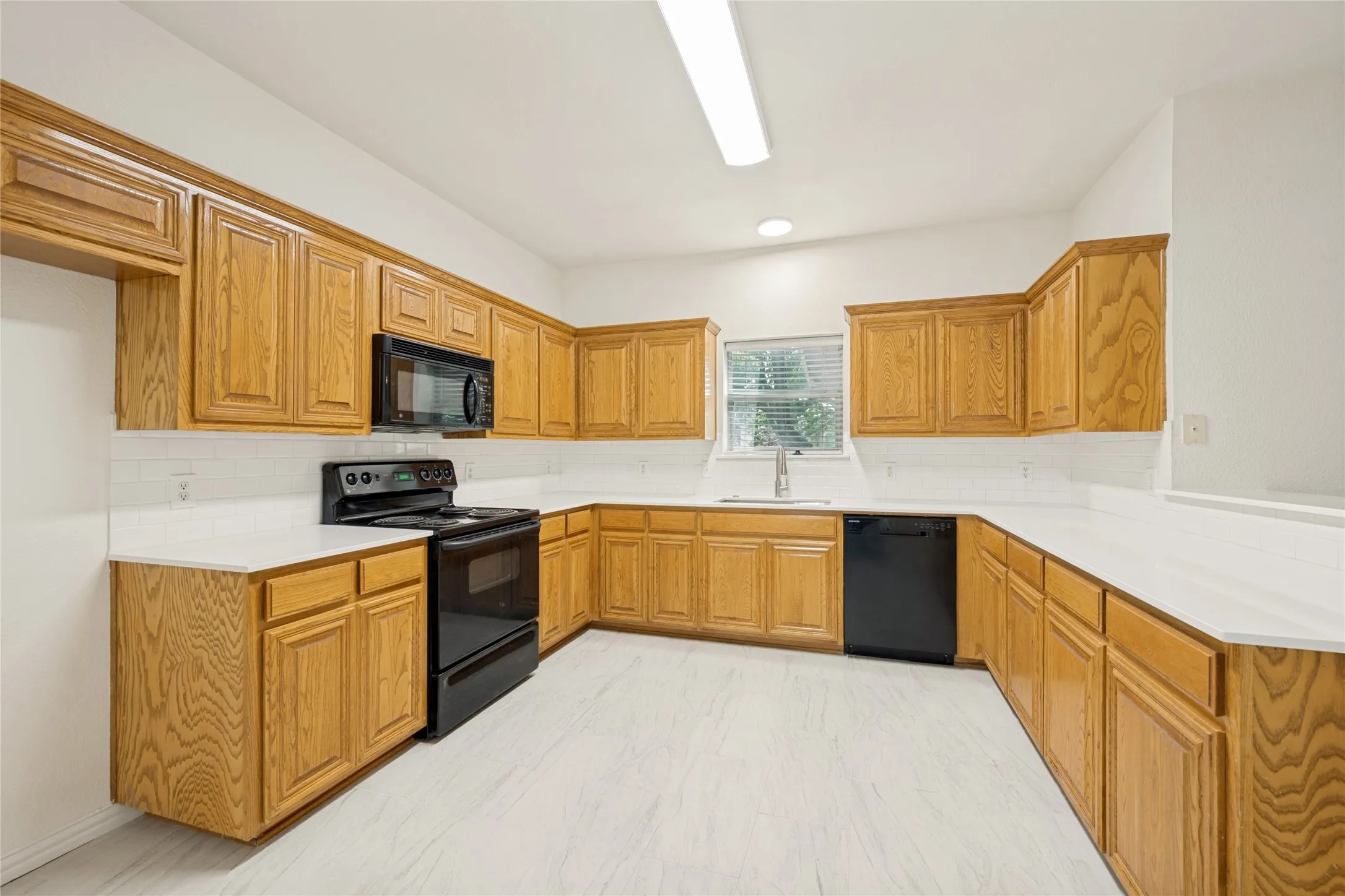 Kitchen featuring abundant wood cabinetry, white countertops, tile backsplash, stainless steel sink with gooseneck faucet, and black appliances including a range, microwave, and dishwasher