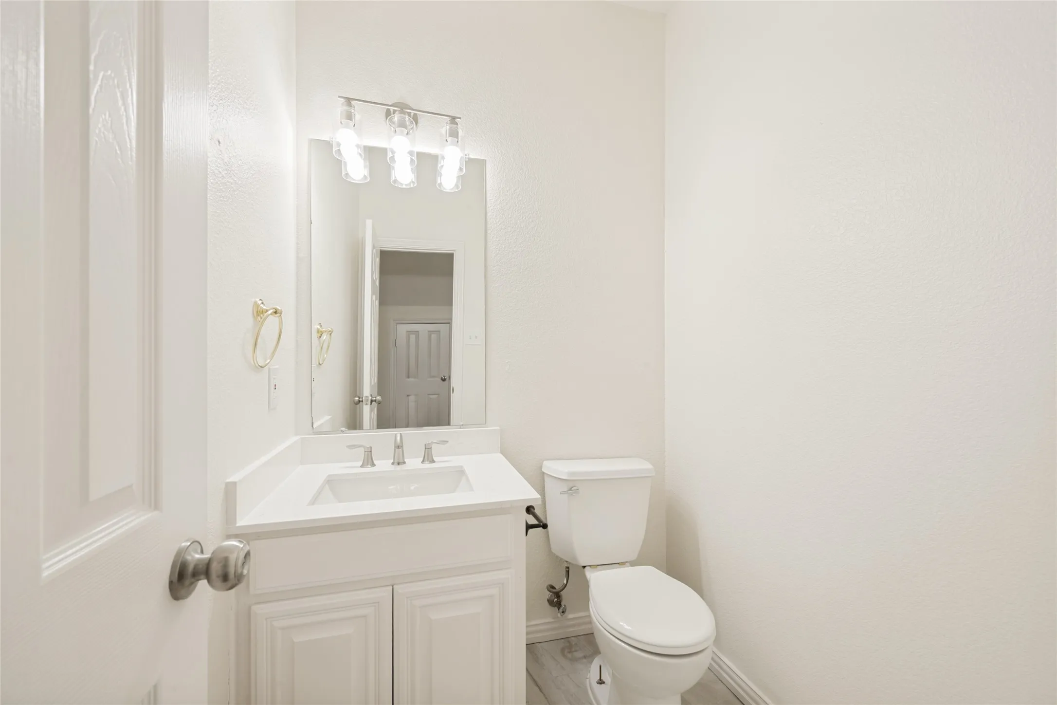 Bathroom featuring a white vanity with built-in sink, brushed nickel faucet, and a wall-mounted mirror with a three-light fixture