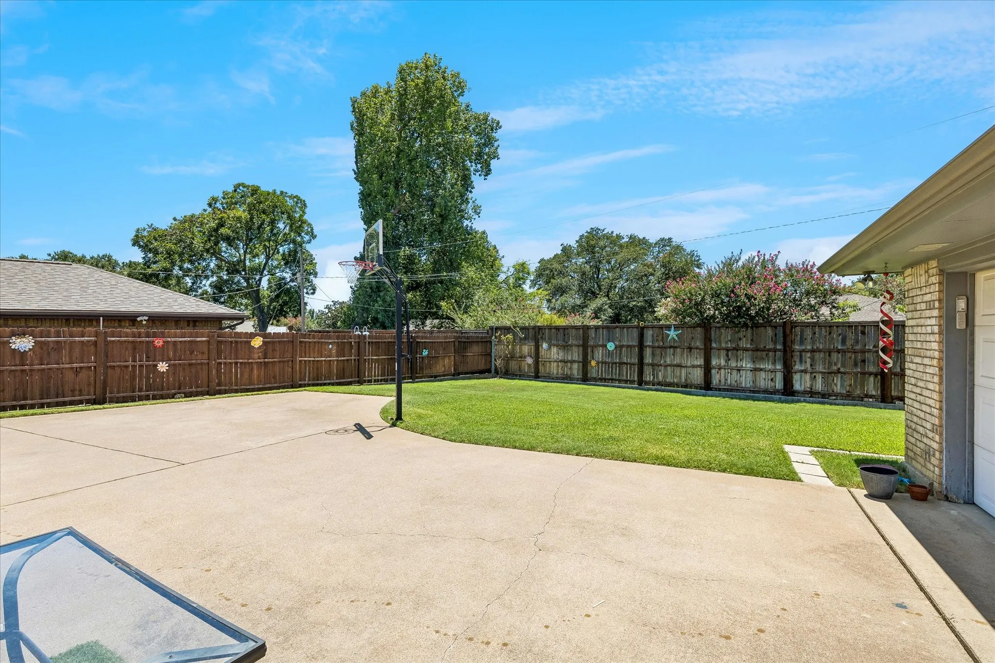 Expansive backyard oasis featuring a generous concrete patio, manicured lawn, mature shade trees, and sturdy wood-finish fencing with metal gate accents