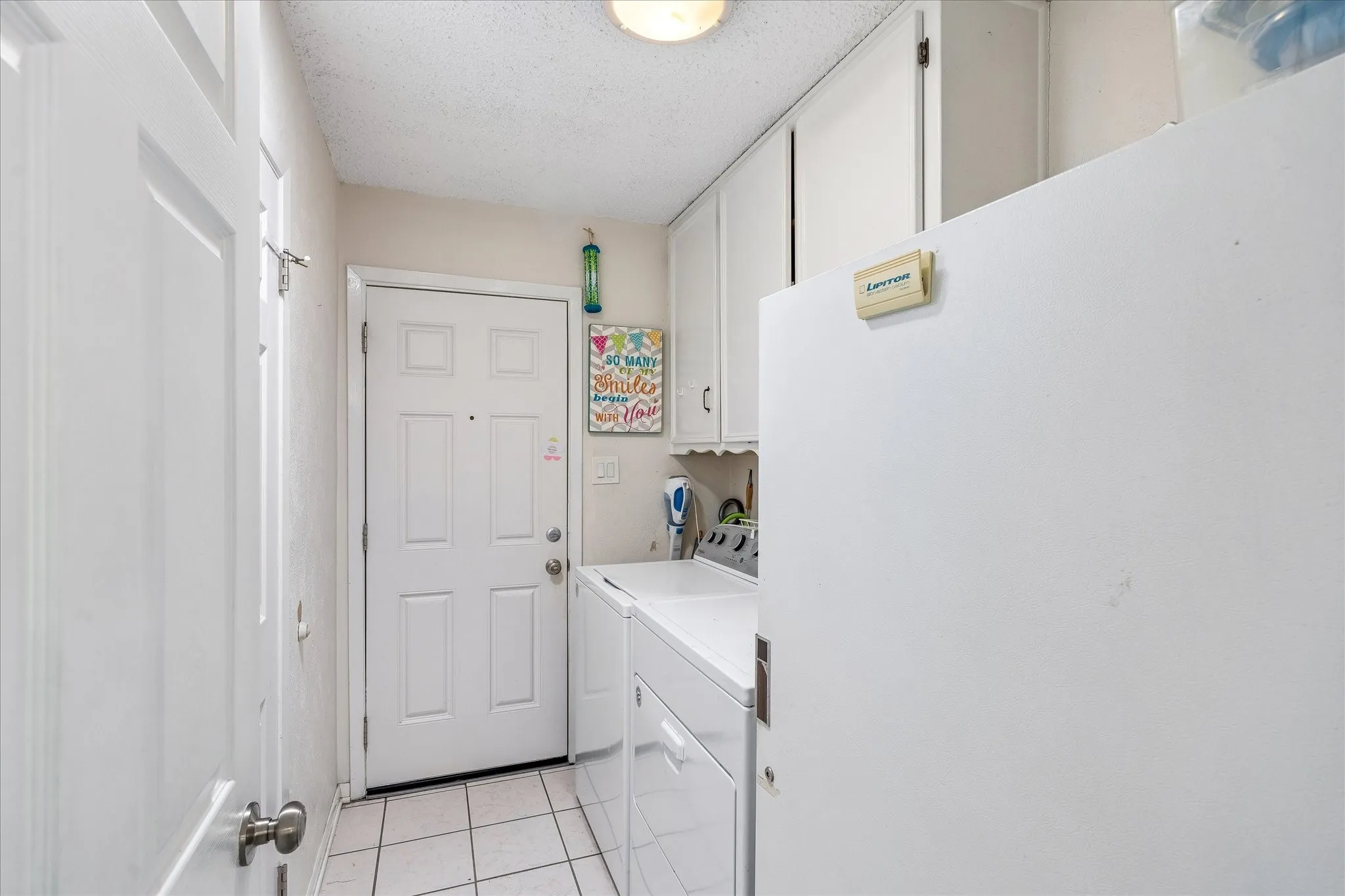 Utility space featuring a paneled door, white tile flooring, white cabinetry, and a white appliance