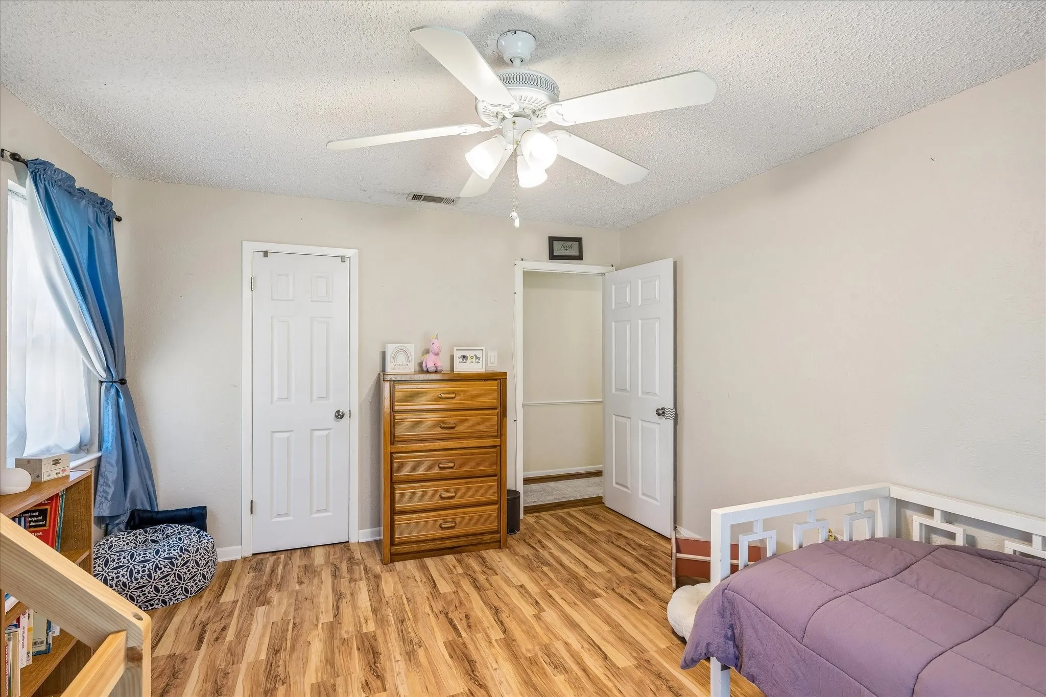 Spacious bedroom featuring wood-finish flooring, a ceiling fan with integrated lighting, and multiple closet options