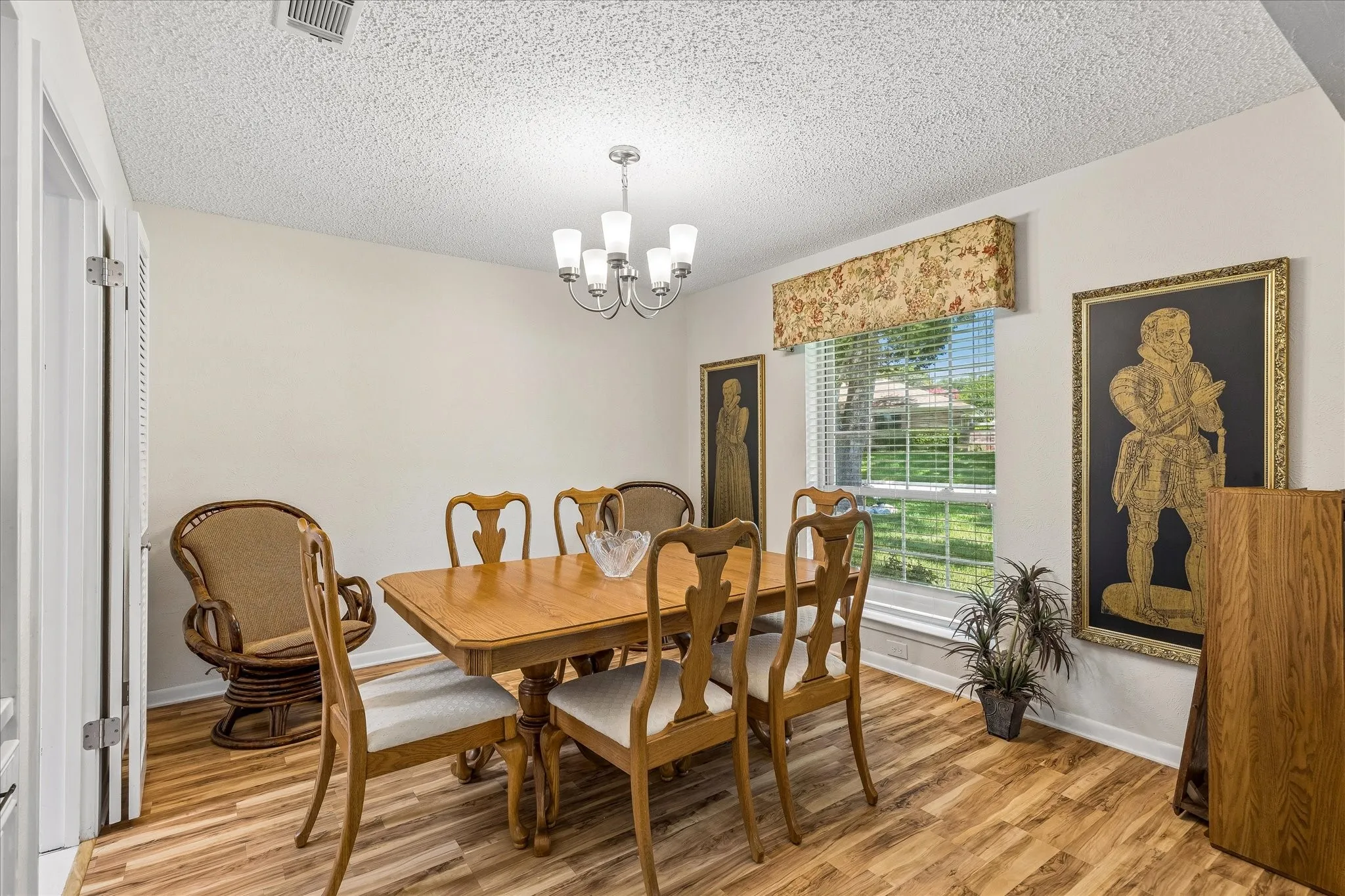 Dining area featuring wood-finish flooring, a contemporary chandelier, a window with blinds and a fabric valance, and a bi-fold door