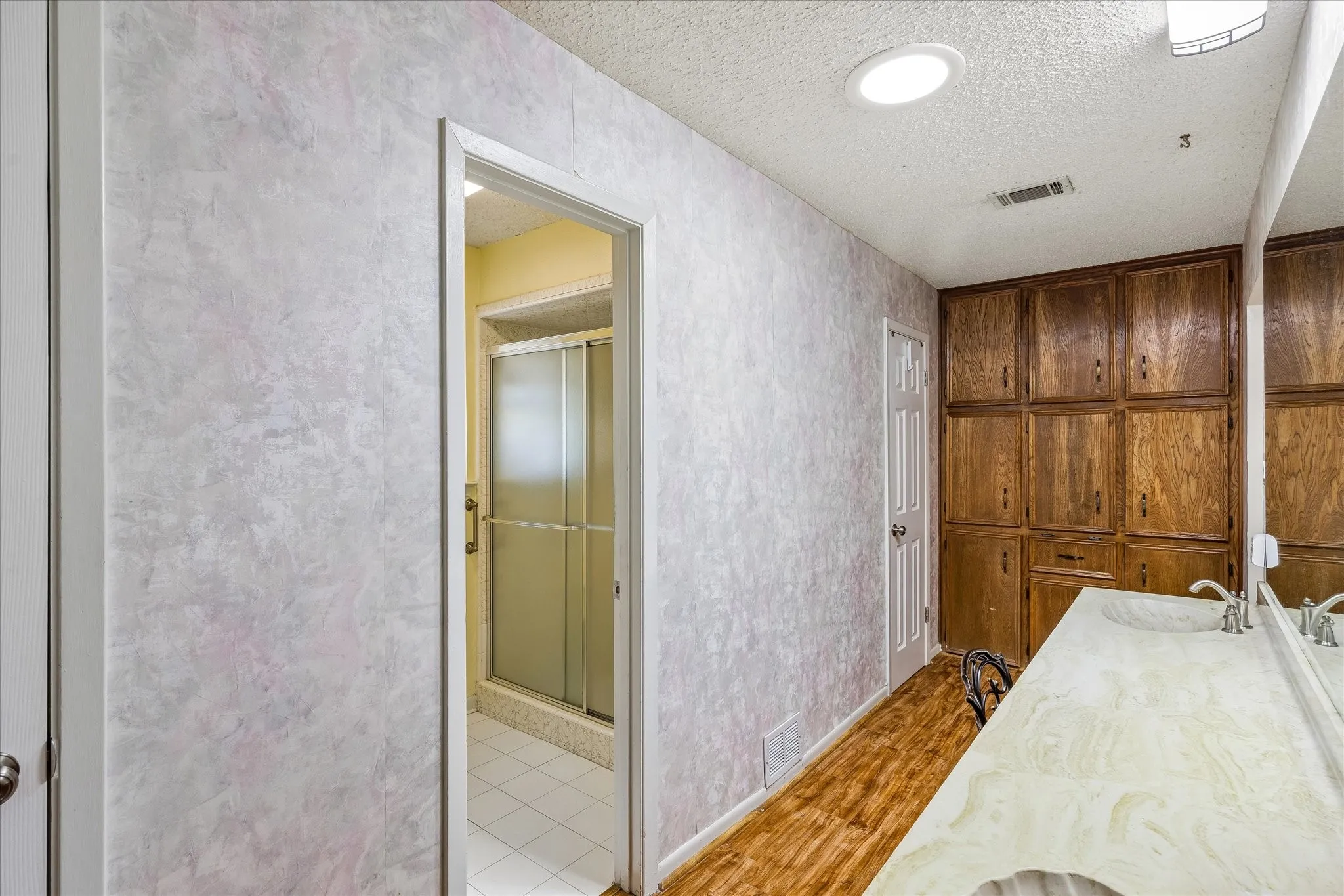 Bathroom featuring a double vanity with integrated sinks and wall-to-wall mirror, extensive built-in wood cabinetry, wood-finish flooring, and a recessed ceiling light
