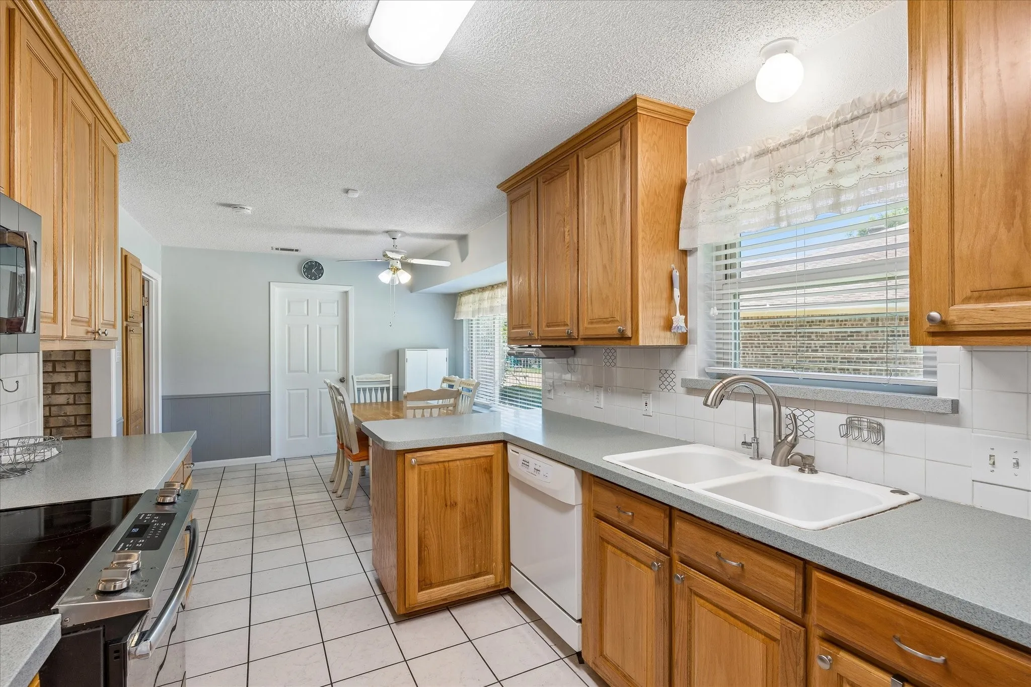 Kitchen featuring wood cabinetry, solid surface countertops, white tile flooring, double basin sink, and a tiled backsplash