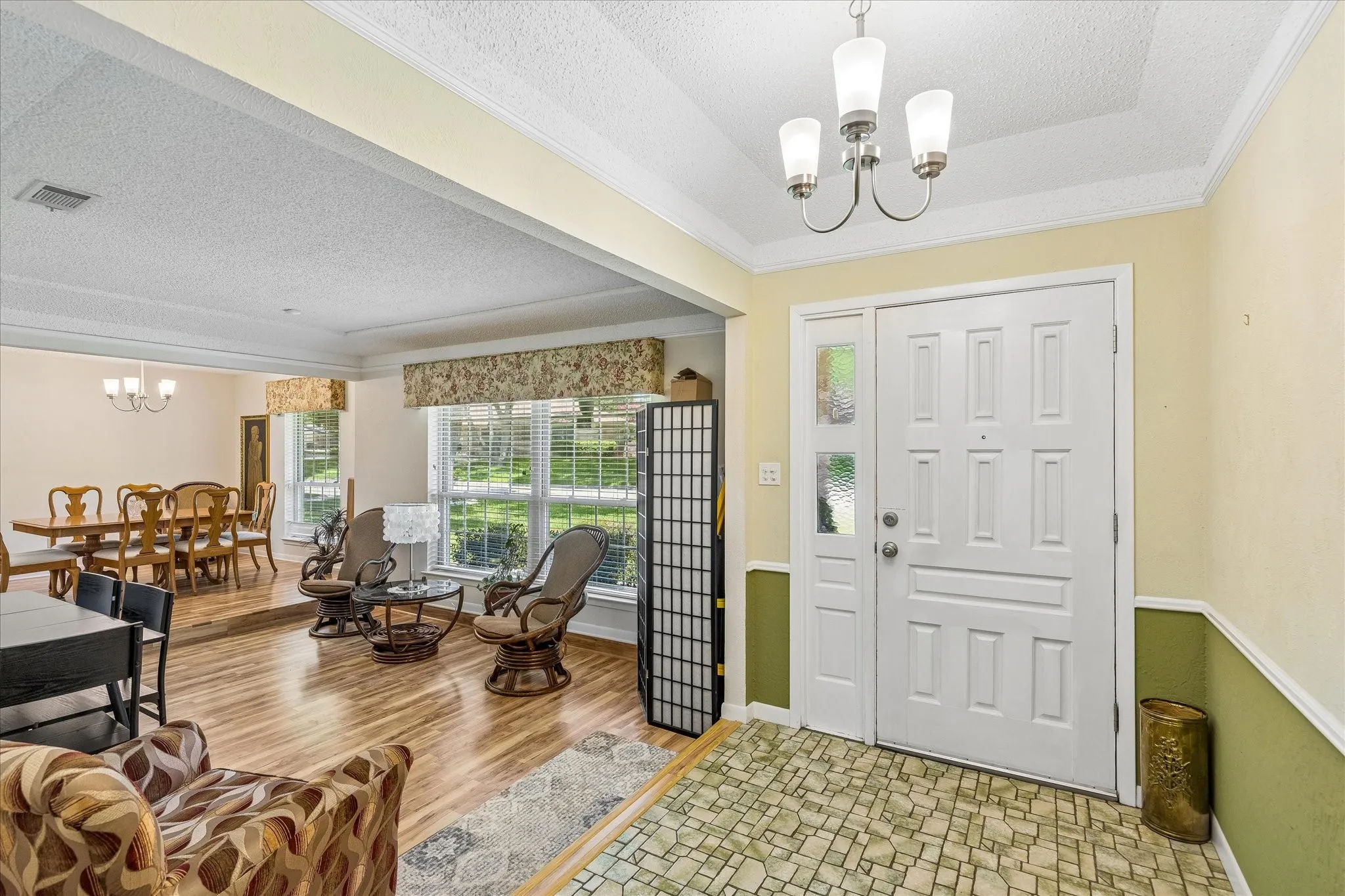 Welcoming foyer featuring dual white six-panel doors, warm yellow walls with green wainscoting, and wood-finish flooring