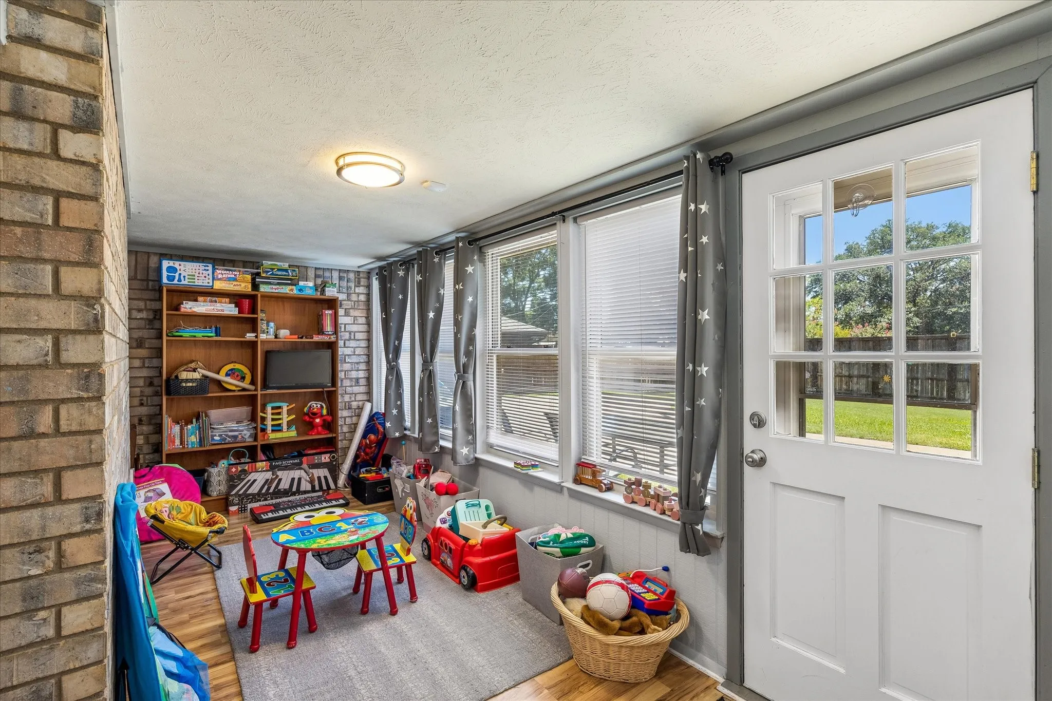 Bright sunroom with sliding glass doors opening to outdoor grounds, featuring built-in shelving with wood-finish cabinetry, recessed ceiling lighting, and gray tile flooring