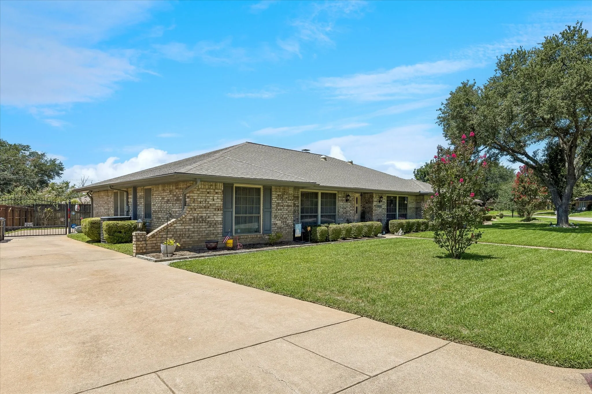 Brick exterior featuring a hip roof, mature trees, and a concrete driveway