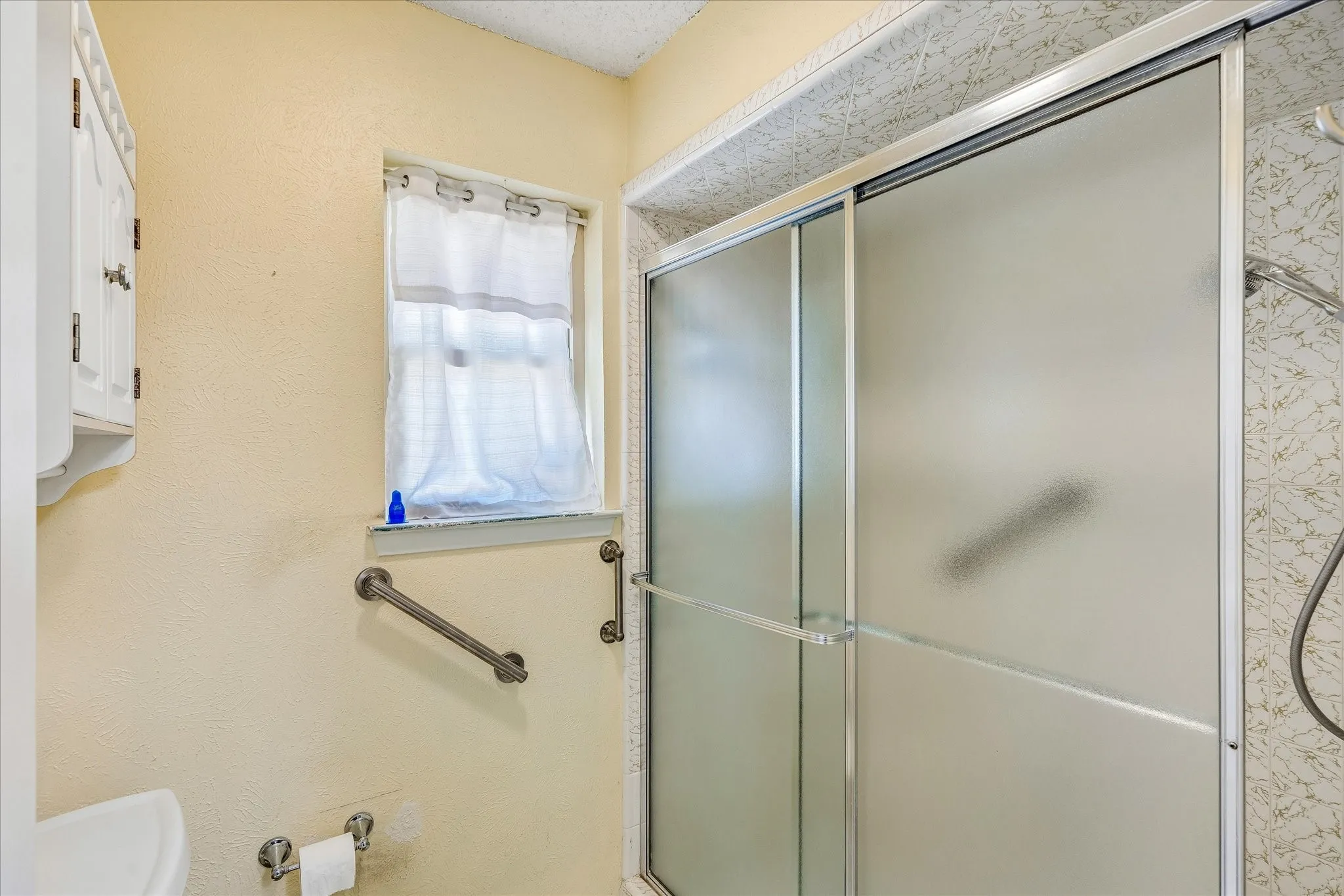 Shower enclosure with frosted sliding glass doors and grab bars