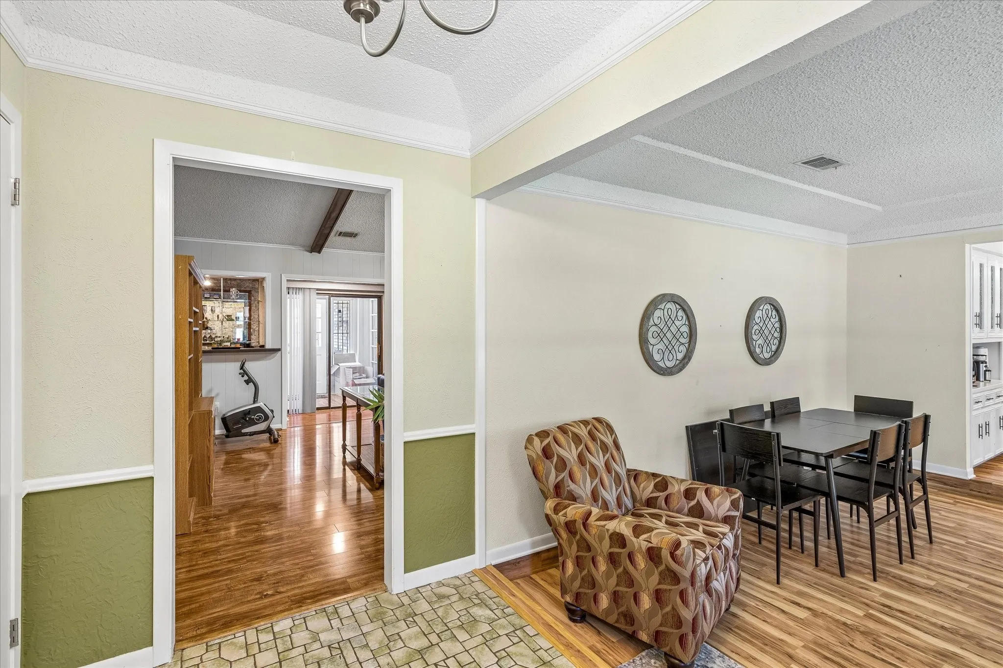 Open floor plan featuring warm wood-finish flooring, neutral wall palette with sage green wainscoting accents, and abundant natural light