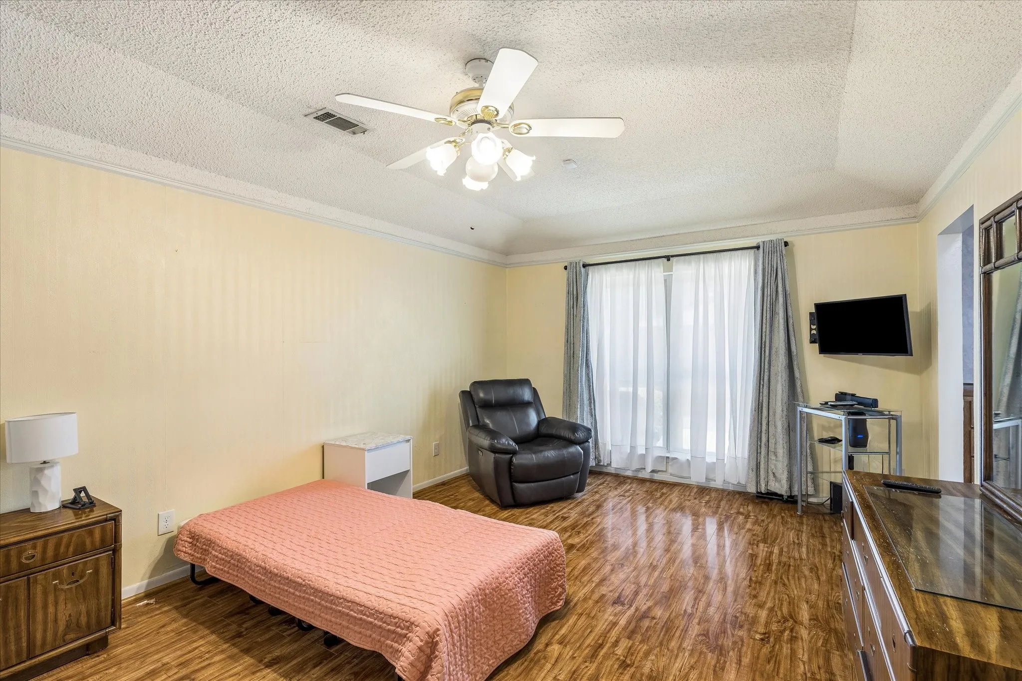 Spacious bedroom featuring wood-finish flooring, ceiling fan with integrated lighting, and glass sliding door access