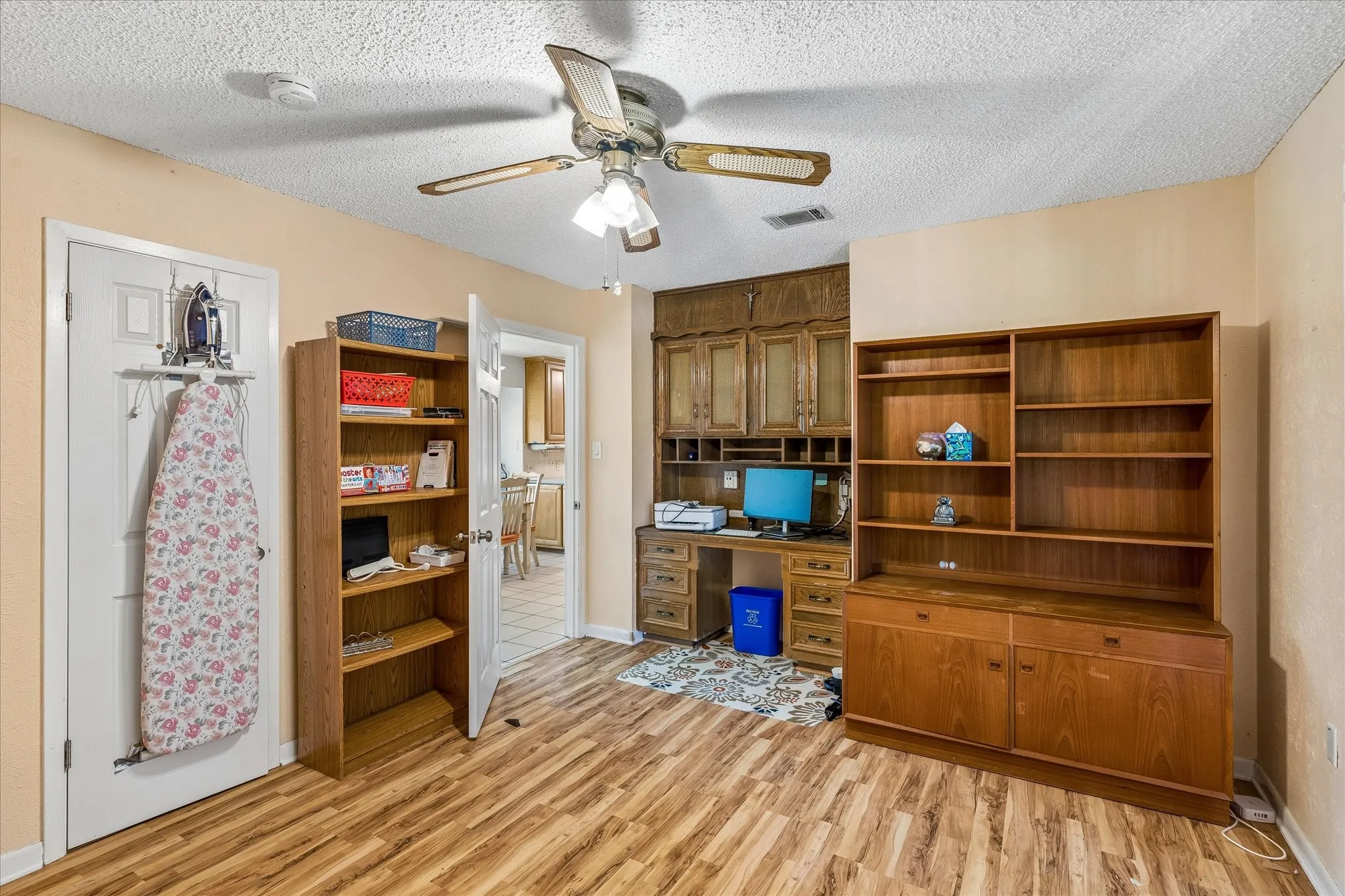 Room featuring wood-finish flooring and a built-in wooden desk with upper cabinetry